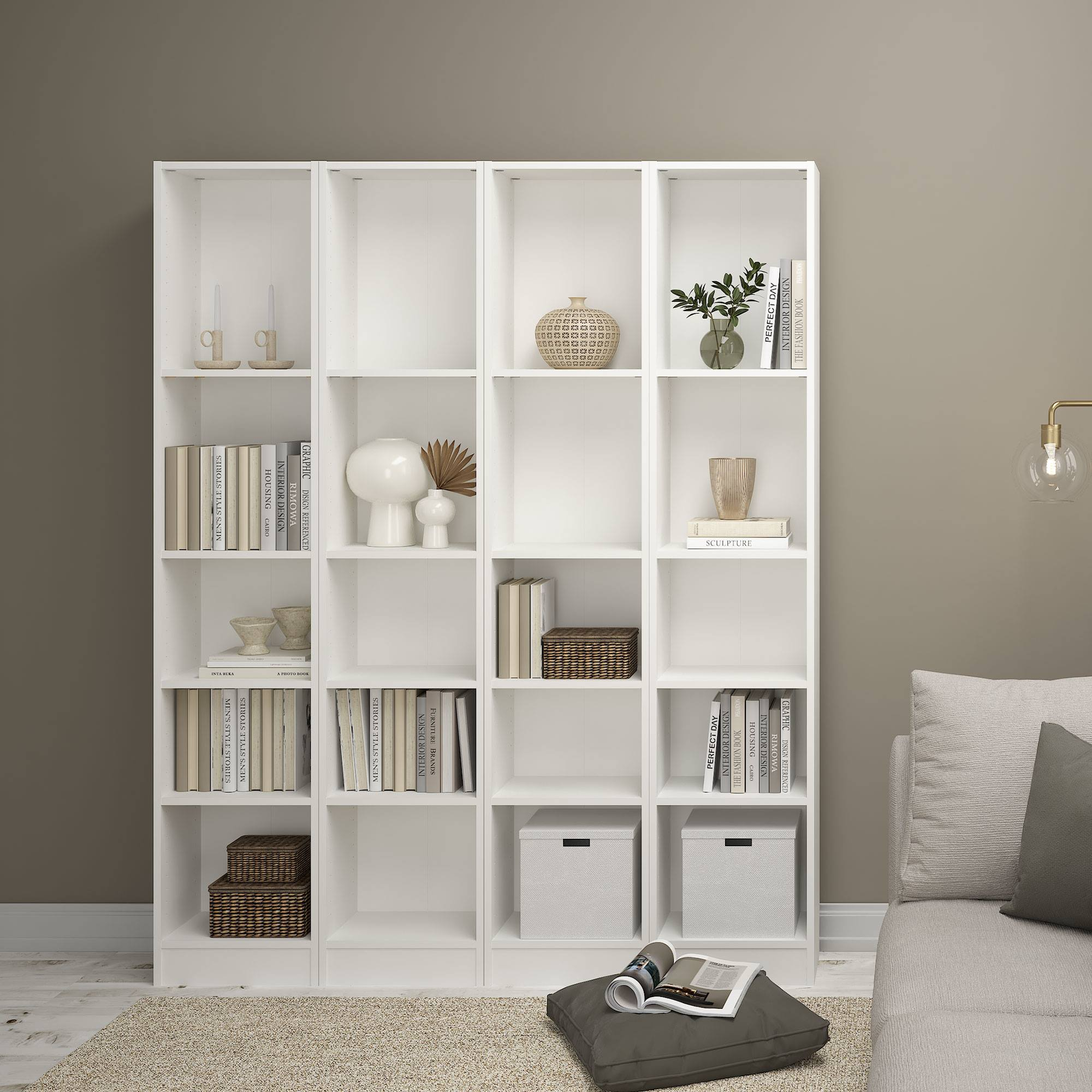 Librería blanca llena de libros, jarrones y objetos decorativos. Un sofá está al fondo.
