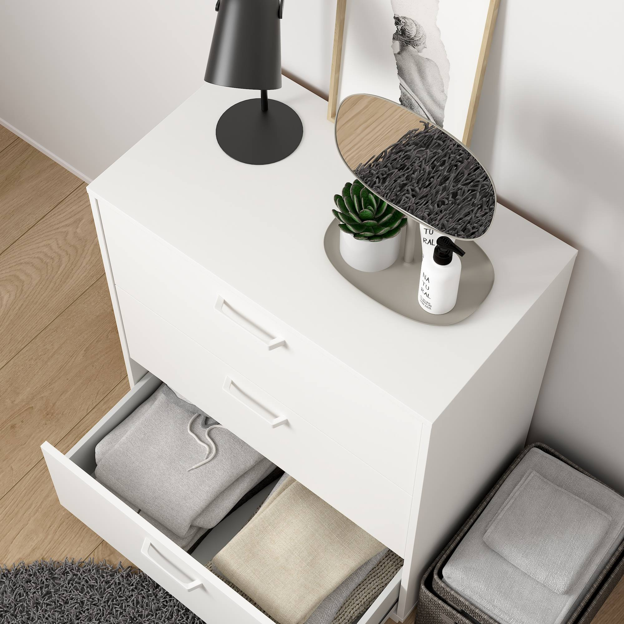 Cómoda blanca con cajones abiertos, lámpara, espejo, planta y toallas. Los cajones contienen ropa doblada.