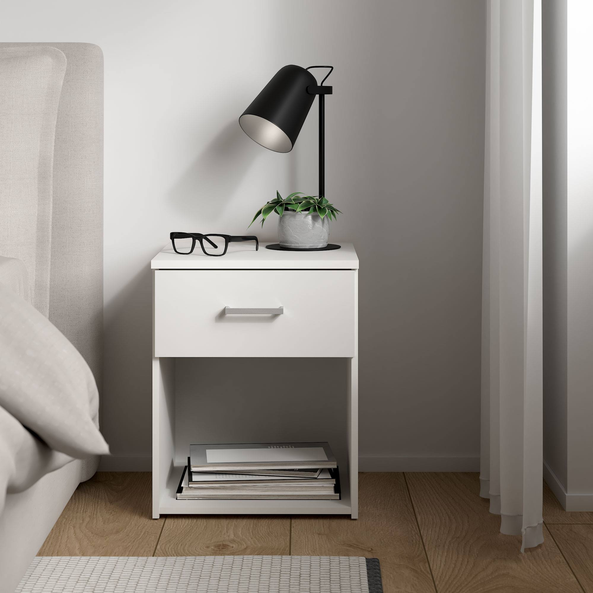 Una mesita de noche blanca con lámpara, planta y gafas. Hay una cama a la izquierda. Libros en el estante inferior.