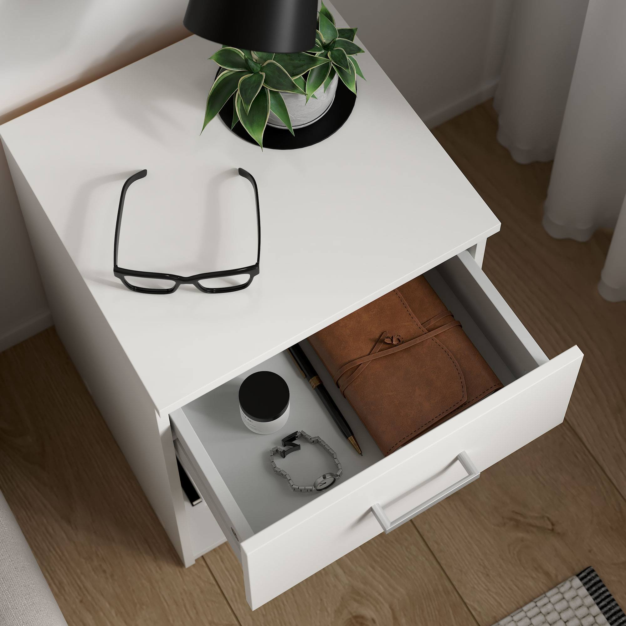 Mesita de noche blanca con cajón abierto. Dentro: cuaderno, bolígrafo, reloj, tarro. Gafas arriba. Planta y lámpara arriba.