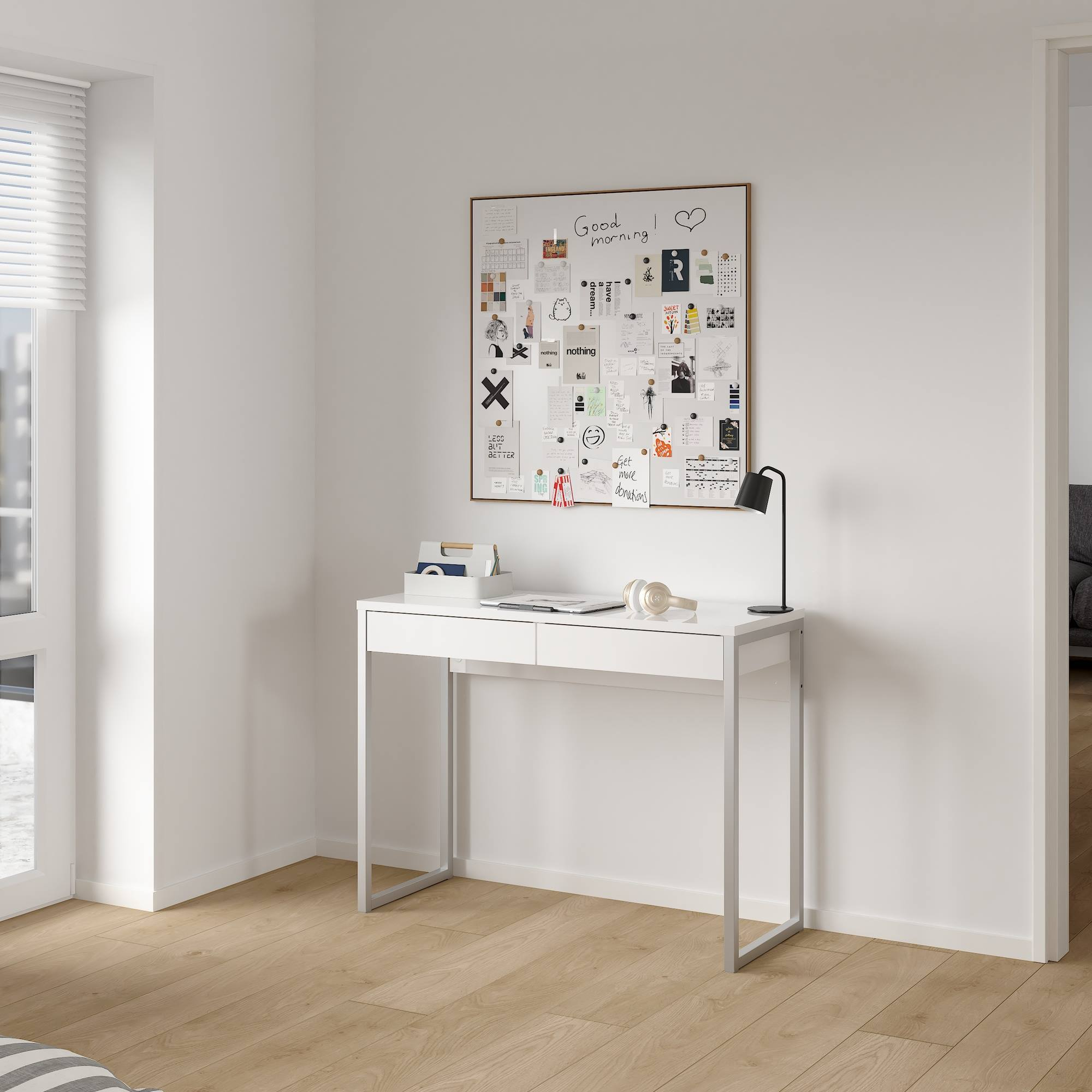 Un escritorio blanco con un tablón de anuncios, una lámpara y auriculares. El escritorio está en una habitación luminosa con suelos de madera.