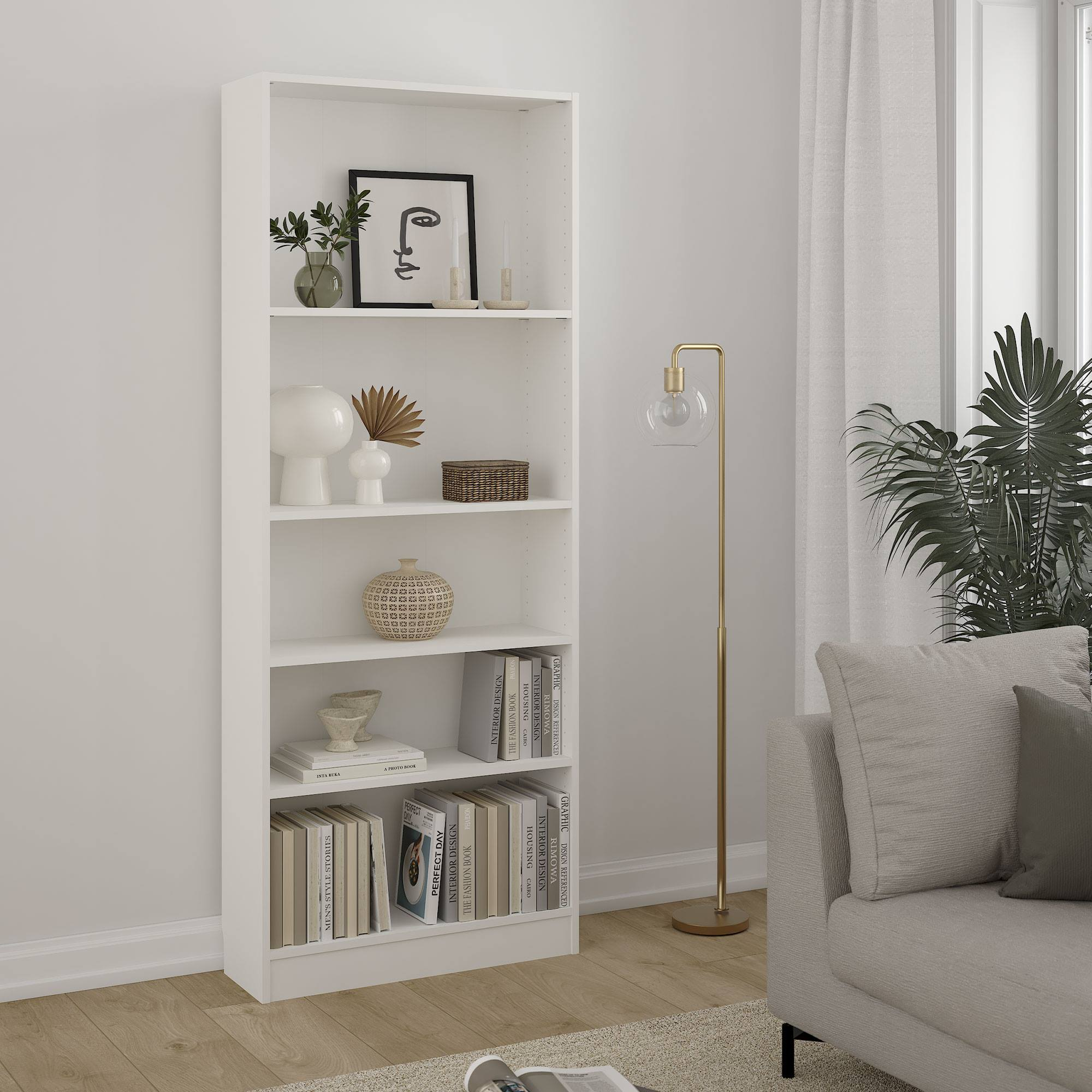 Una estantería blanca está llena de decoración y libros. Una lámpara y un sofá están a la derecha. Una planta grande está al lado de una ventana.