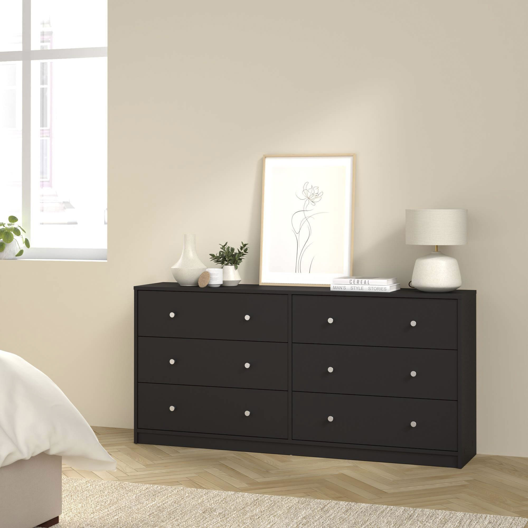 Cómoda negra con objetos encima, junto a una ventana. Una cama está en primer plano.