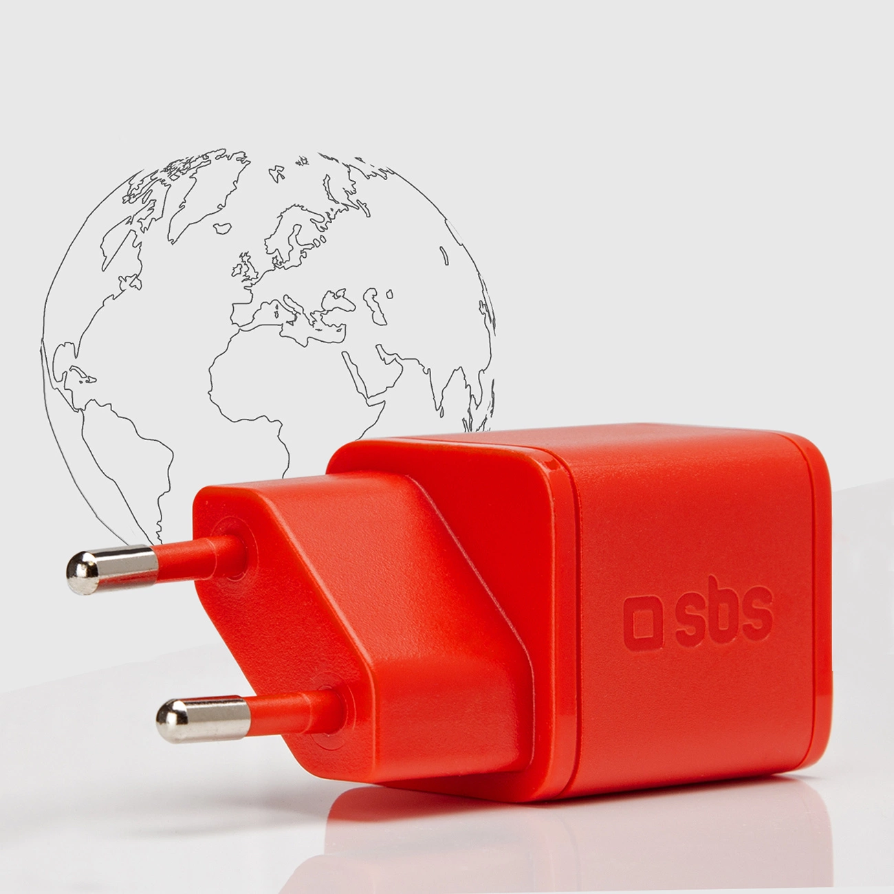 Un adattatore di alimentazione rosso con spine argentate è posto davanti a un globo disegnato. L'adattatore ha il logo 'sbs'.