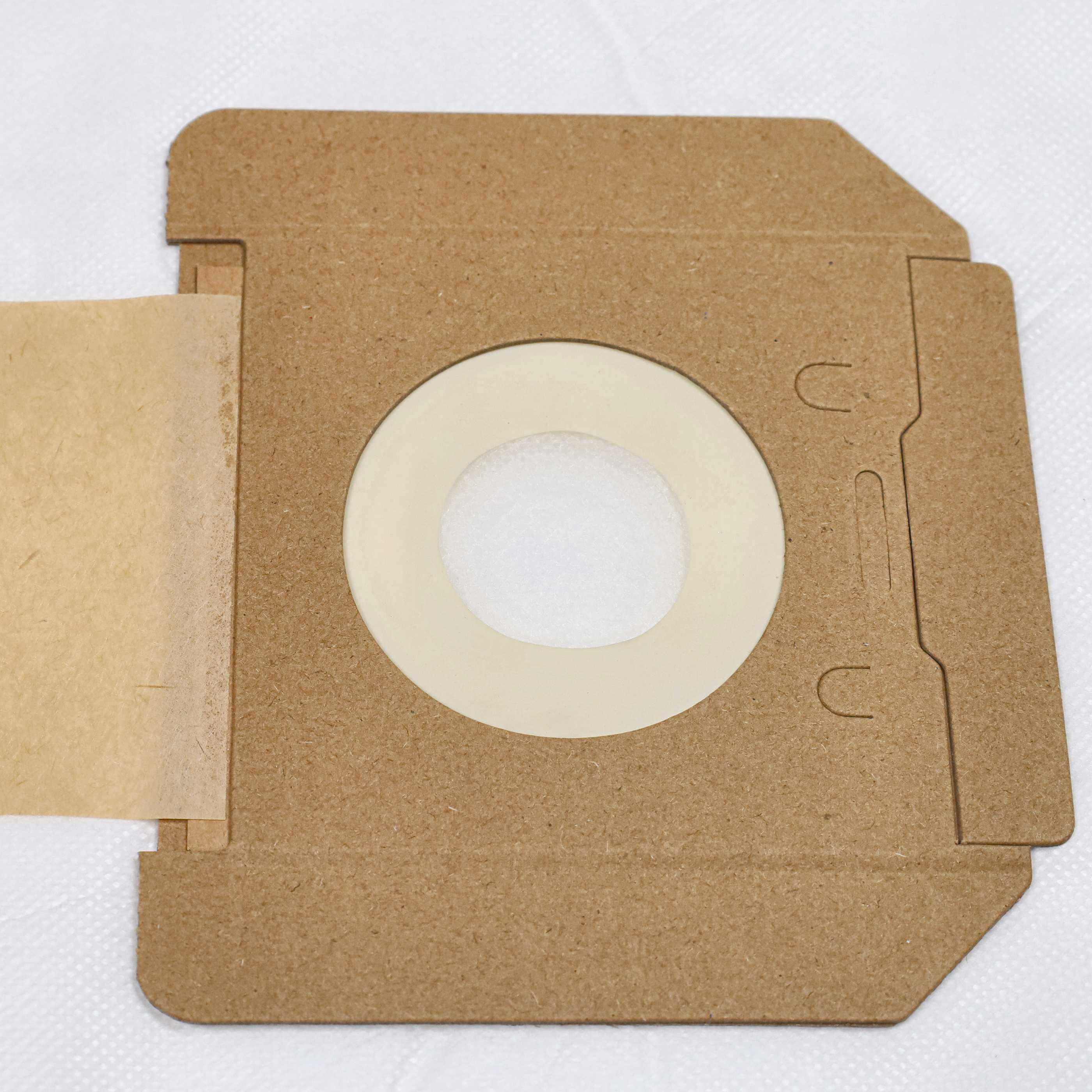 Ein brauner Staubsaugerbeutel mit einer zentralen kreisförmigen Öffnung und einer beigefarbenen Papierverlängerung auf weißem Stoff.