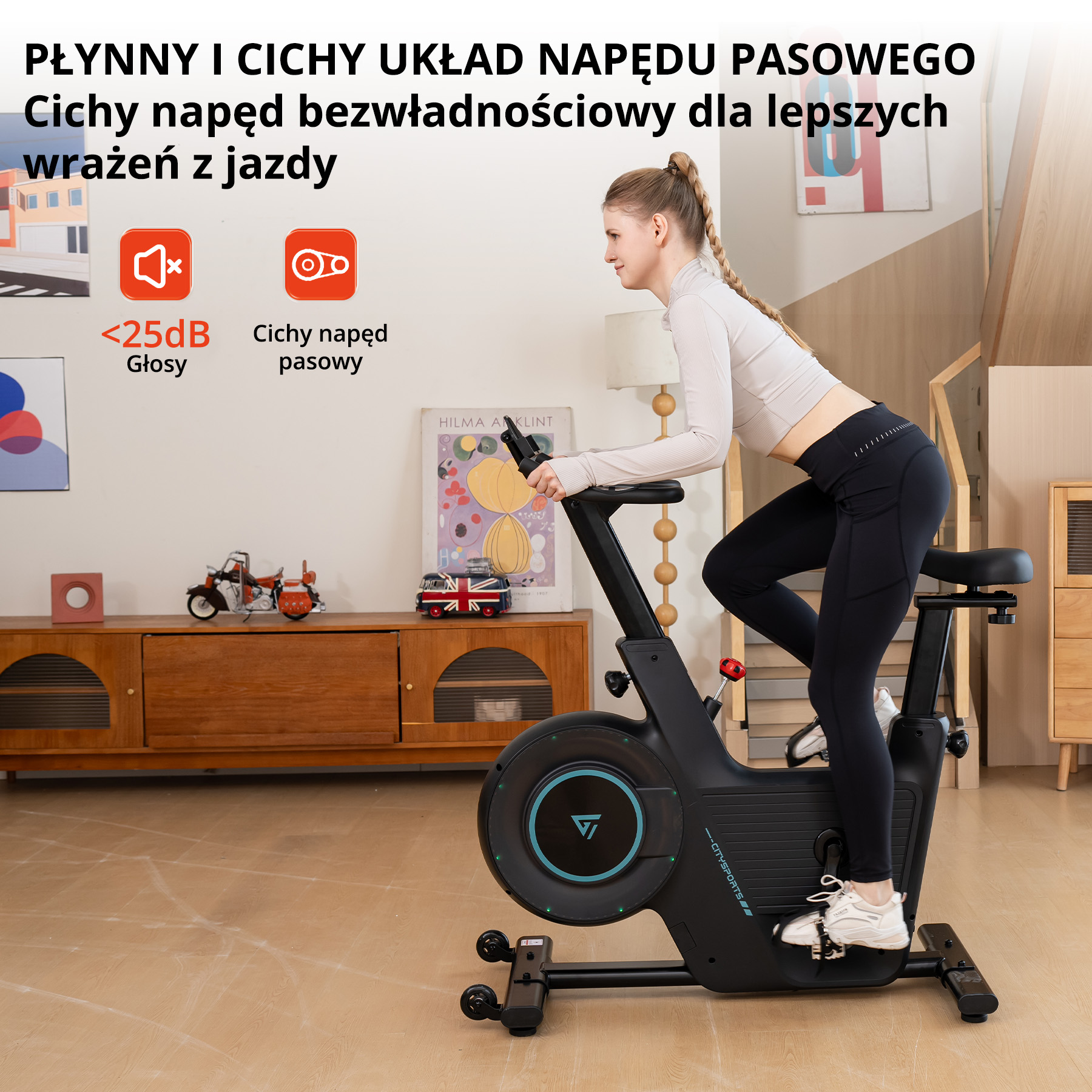 Kobieta ćwiczy na rowerze stacjonarnym w pomieszczeniu. Rower jest czarny i turkusowy. Tło obejmuje meble.