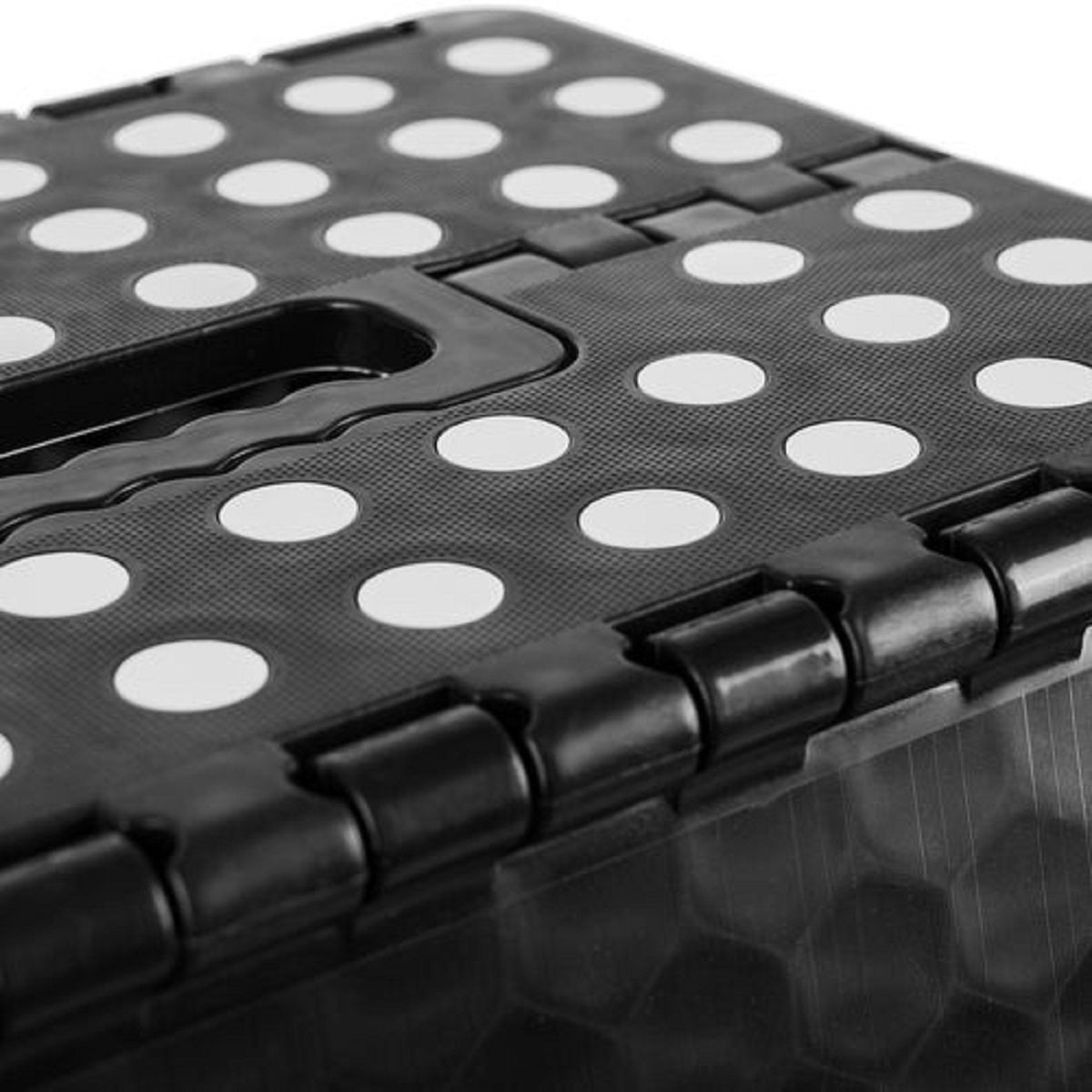 Primer plano de un taburete plegable negro. Tiene agarres circulares blancos y un asa negra. Las bisagras son visibles.