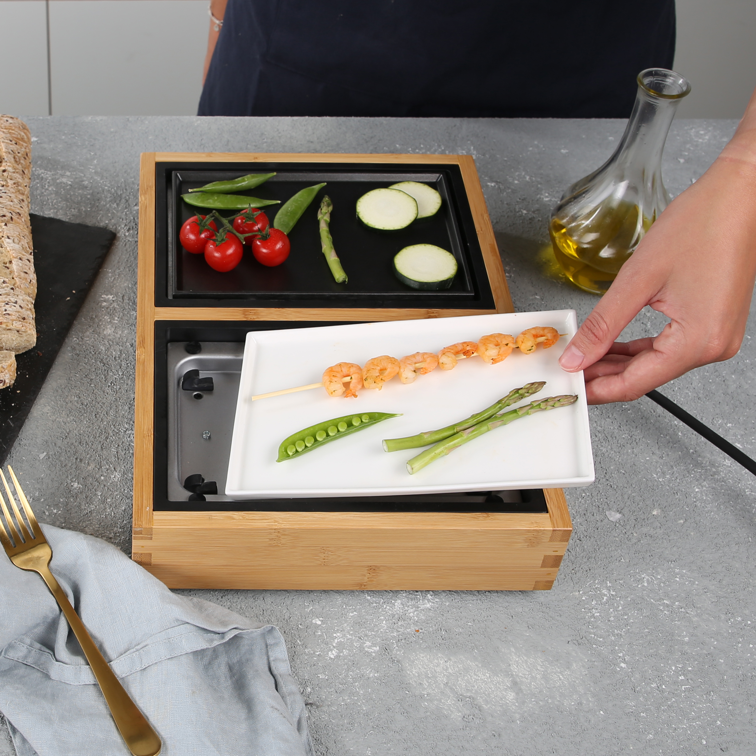 Ein Grill-Setup mit Gemüse, Garnelenspießen und Öl. Eine Hand hält einen Teller mit Essen.