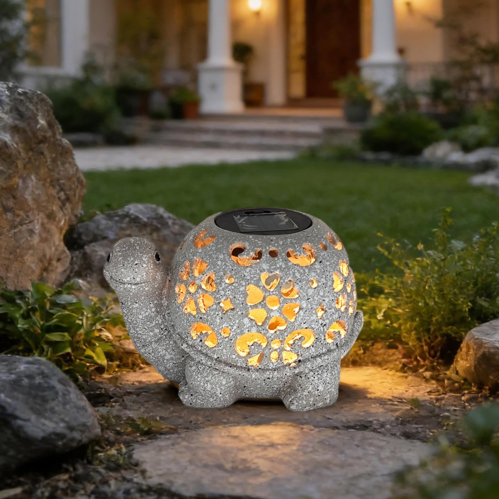 Eine Gartenleuchte aus Stein in Schildkrötenform mit Aussparungen, beleuchtet. Im Hintergrund ein Haus.