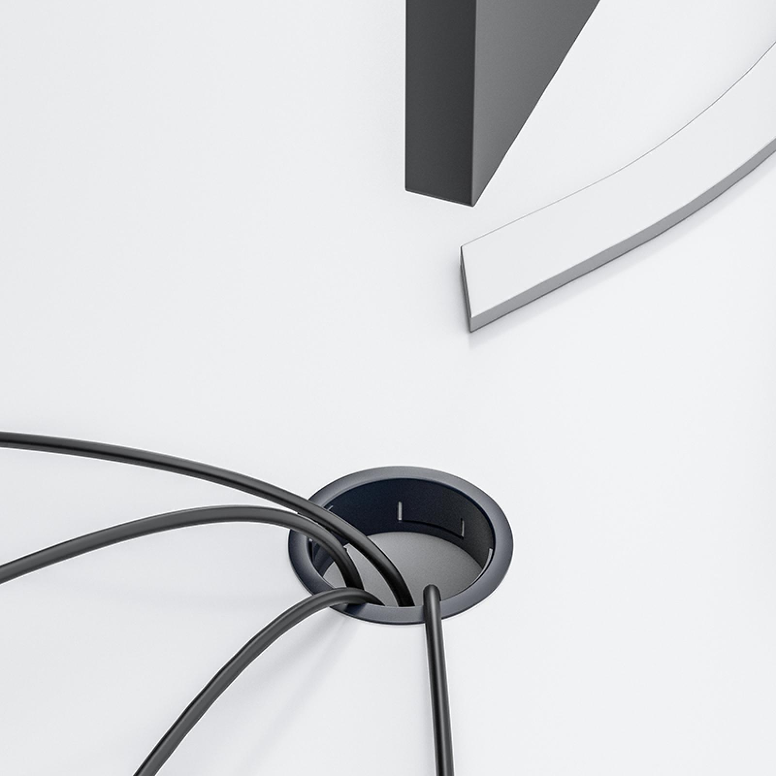 Schwarze Kabel kommen aus einem dunklen Loch auf einer weißen Oberfläche. Eine schwarz-weiße Form ist im Hintergrund.