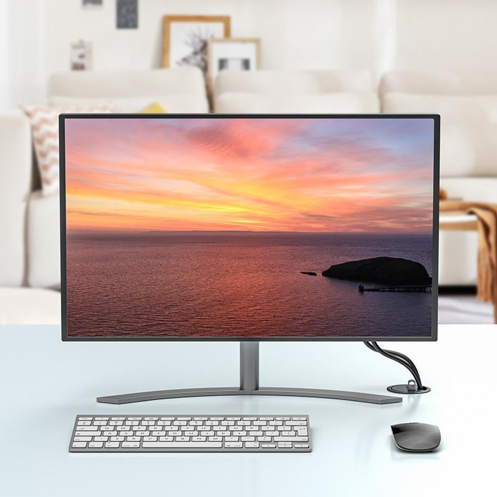Ein Computermonitor zeigt einen Sonnenuntergang über dem Wasser. Tastatur und Maus darunter. Im Hintergrund ein weißes Sofa.
