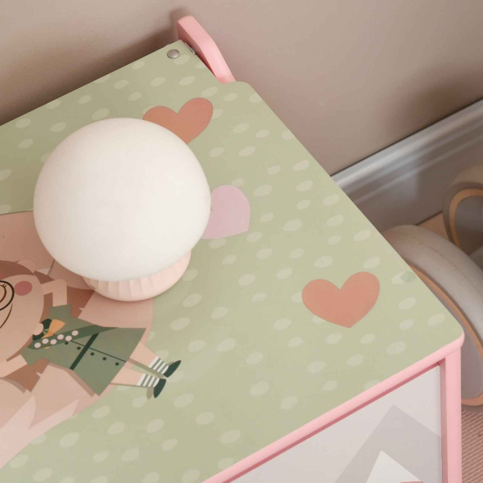 Ein Tisch mit Lampe, grüne Oberfläche mit Herzen und Mädchenillustration. Rosa Rahmen, weiße Punkte.
