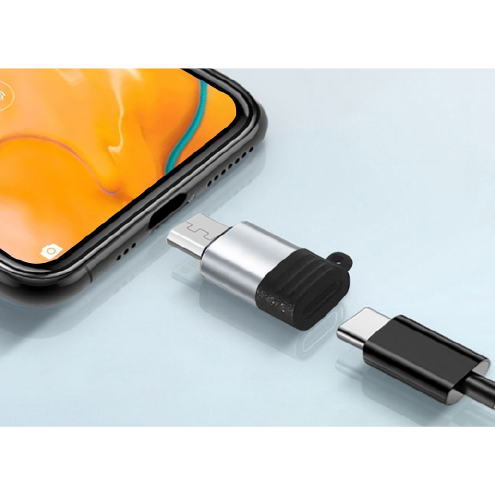 Un teléfono cerca de un adaptador USB y un conector USB-C separado. El adaptador tiene una sección negra y es plateado.