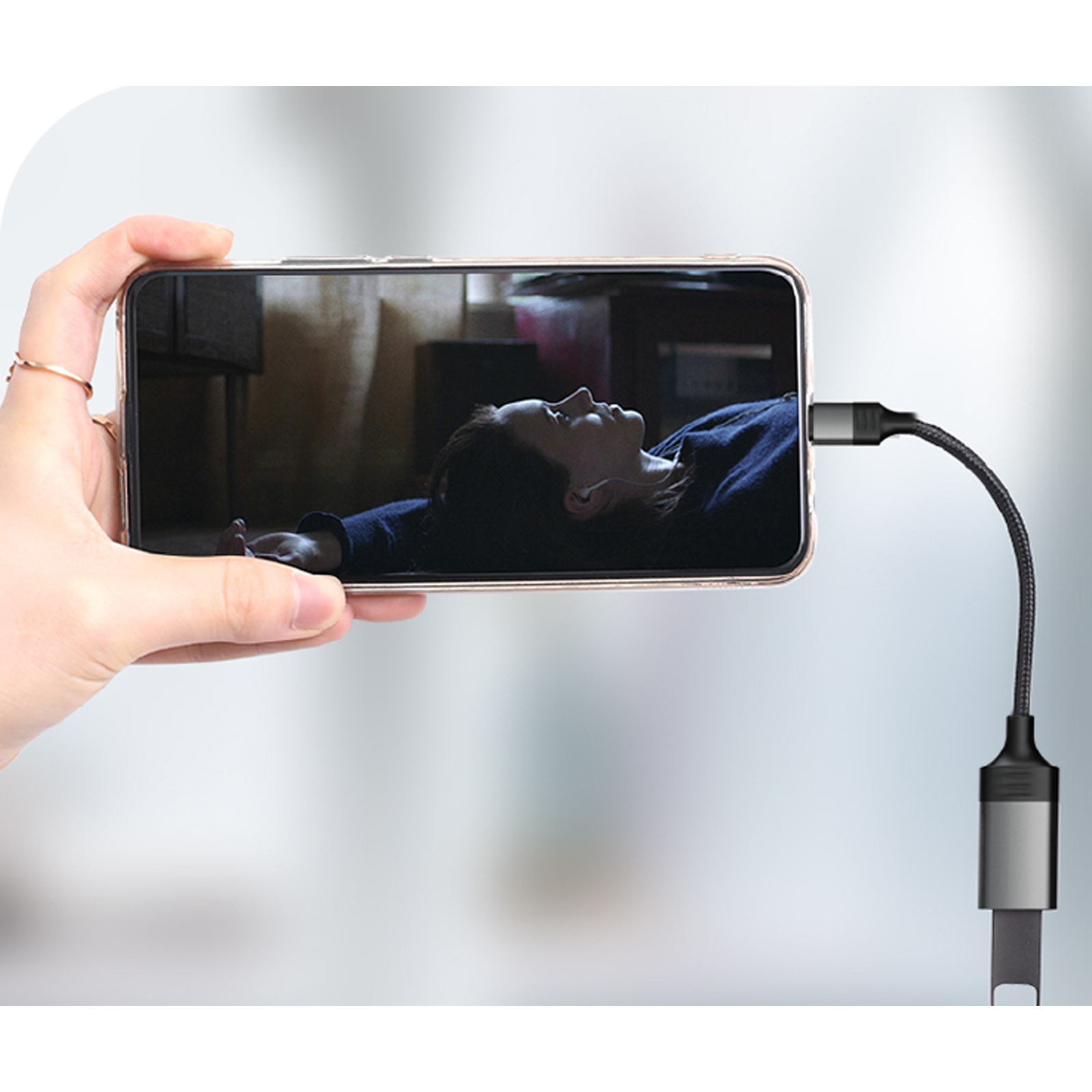 Una mano sostiene un teléfono que muestra a una persona acostada. Un cable se conecta al teléfono.