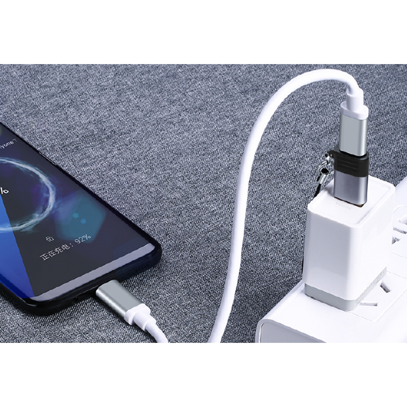Un teléfono se está cargando con un cable blanco conectado a un cargador enchufado a una toma de corriente. El teléfono muestra un 92% de carga.