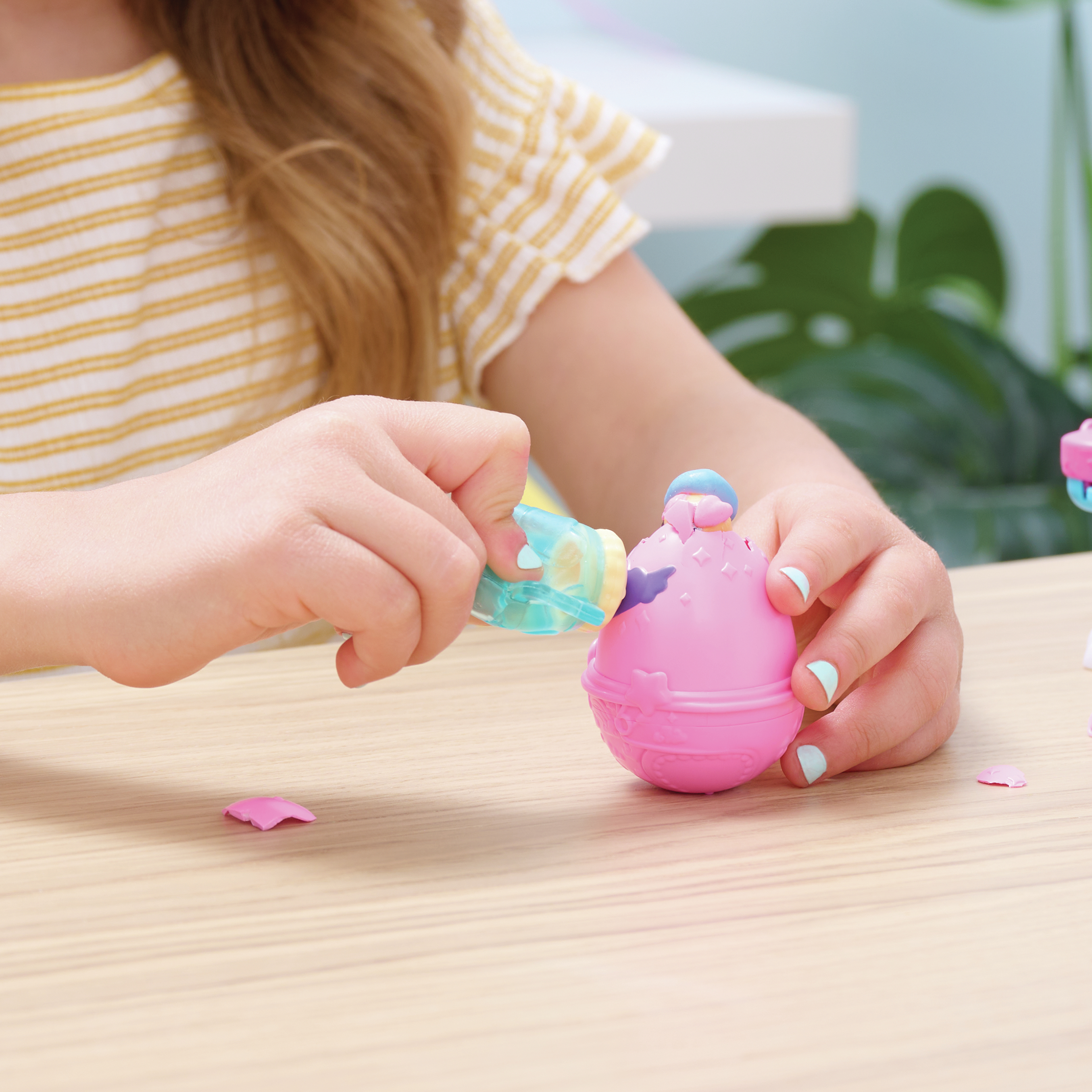 Ein Mädchen öffnet ein rosa Eierspielzeug. Das Ei hat eine blau und rosa Spitze. Die Nägel des Mädchens sind hellblau.