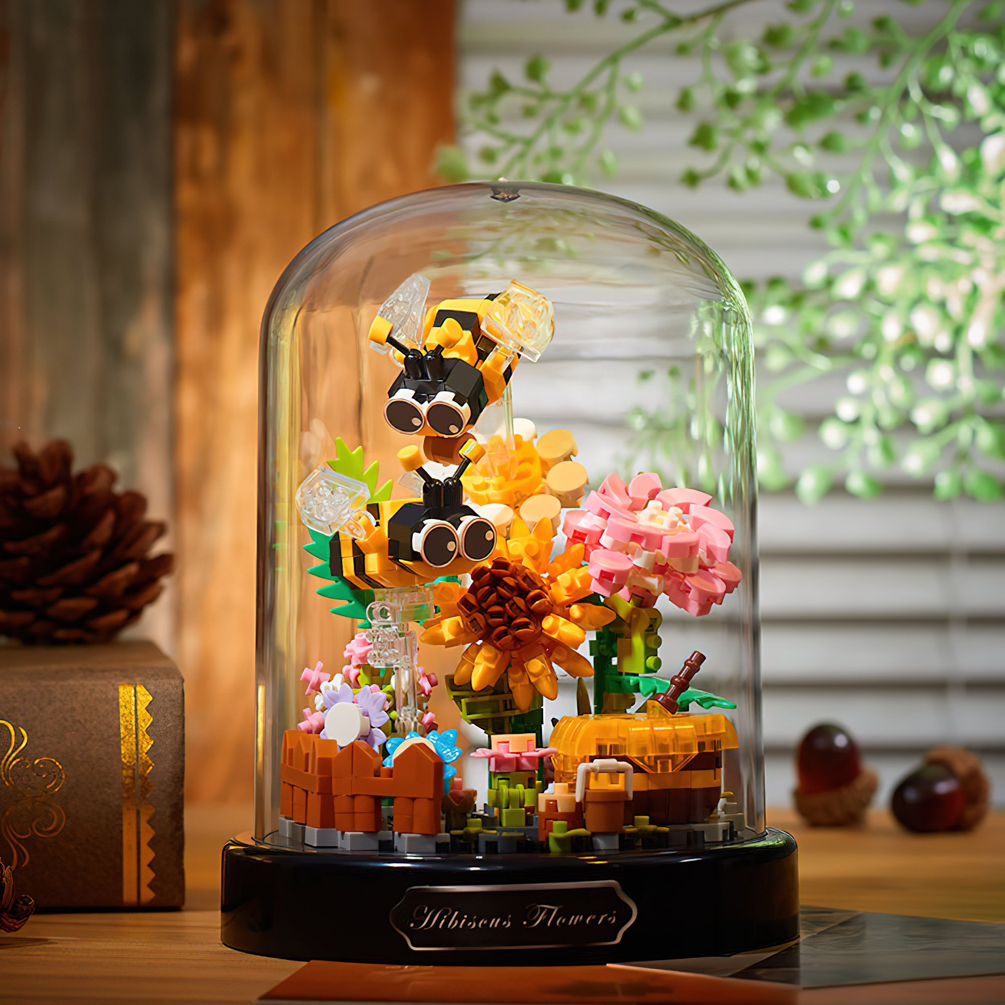 Ein Lego-Diorama aus Blumen und Bienen in einer Glaskuppel. Mit rosa, gelben und orangefarbenen Blumen und einem braunen Sockel.