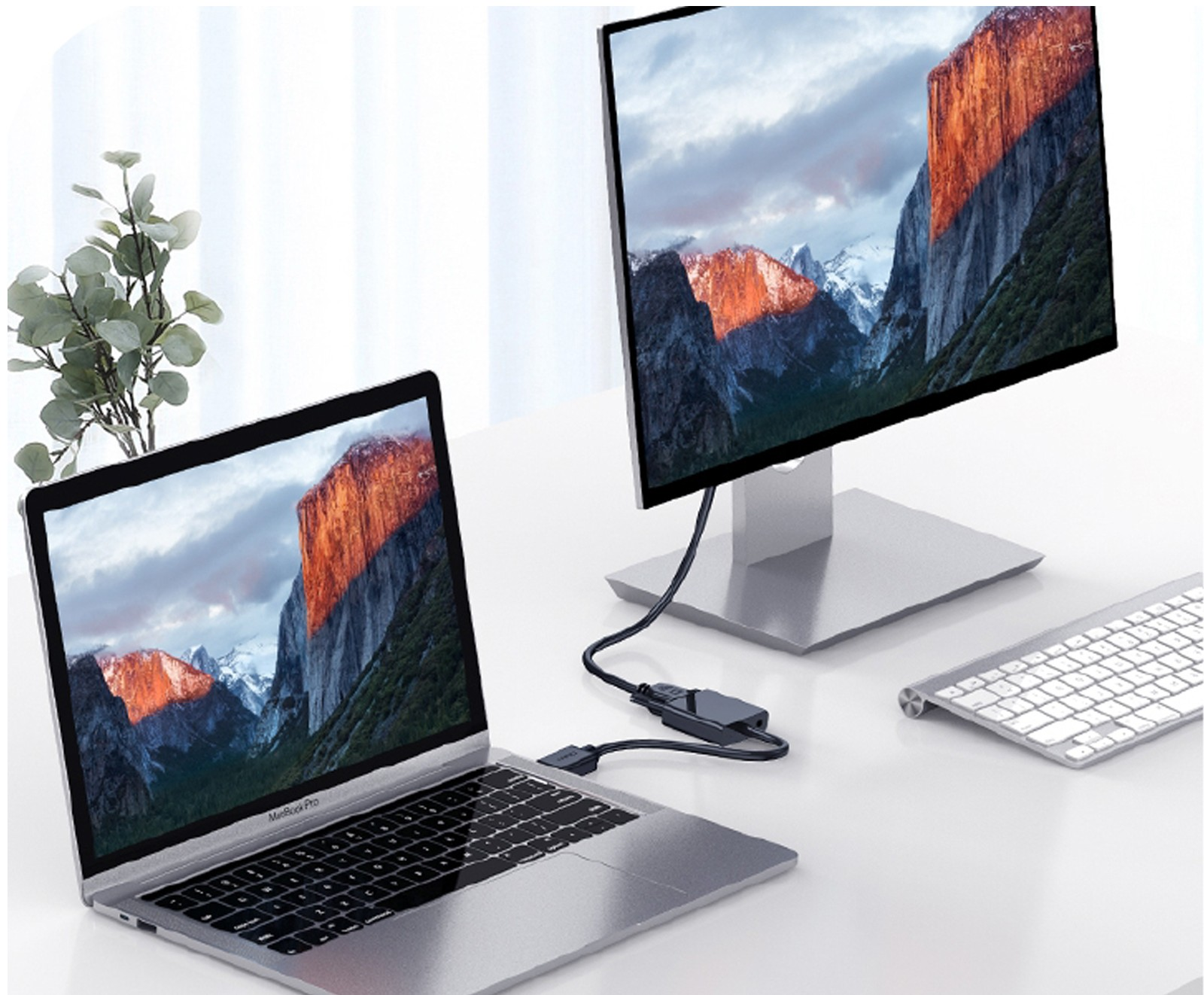 Un portátil y un monitor muestran la misma imagen de montaña. Hay un teclado cerca. Un conector une el portátil y el monitor.