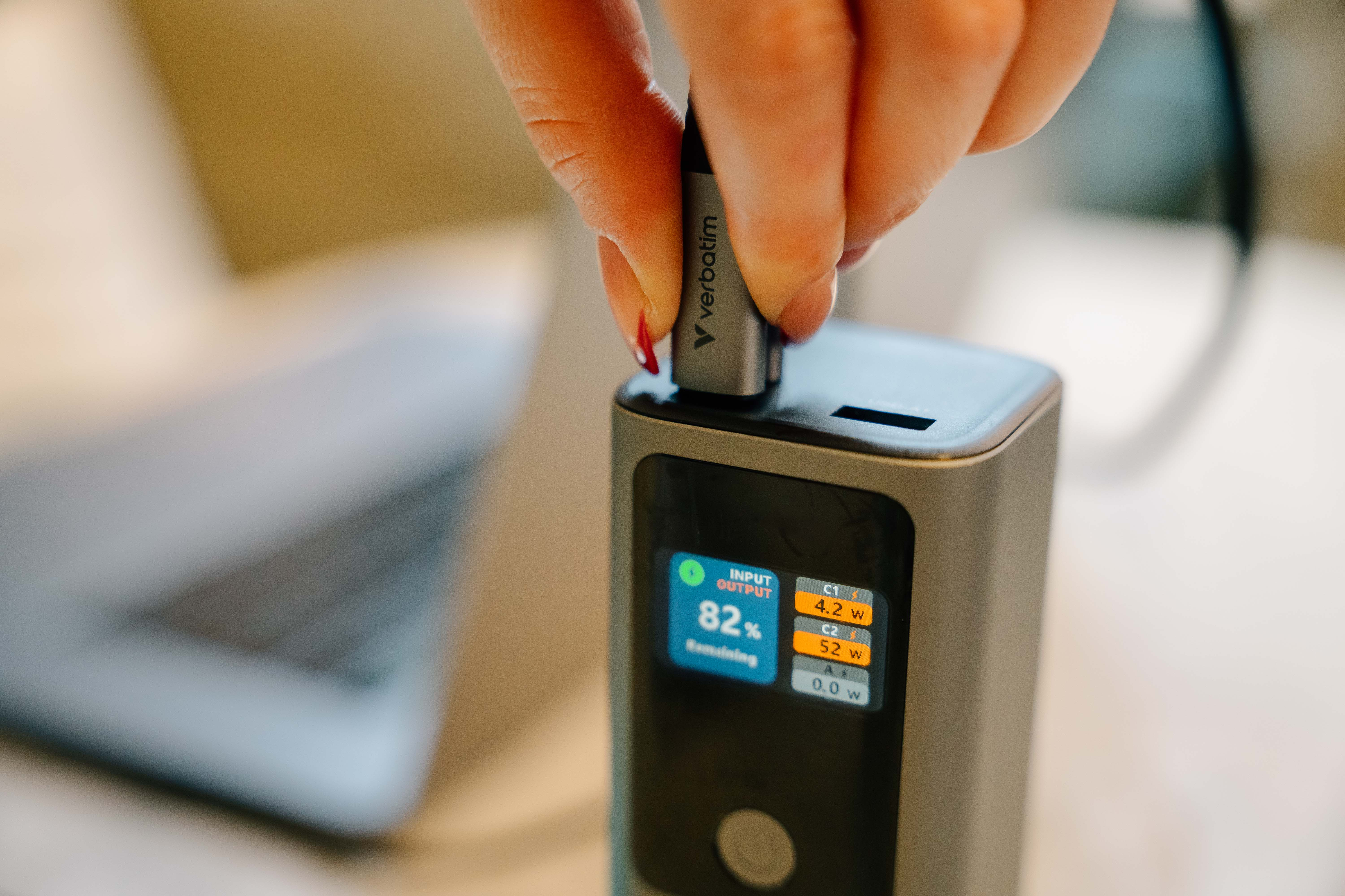 Hand steekt Verbatim USB in powerbank. Scherm toont 82% resterend en outputdetails.