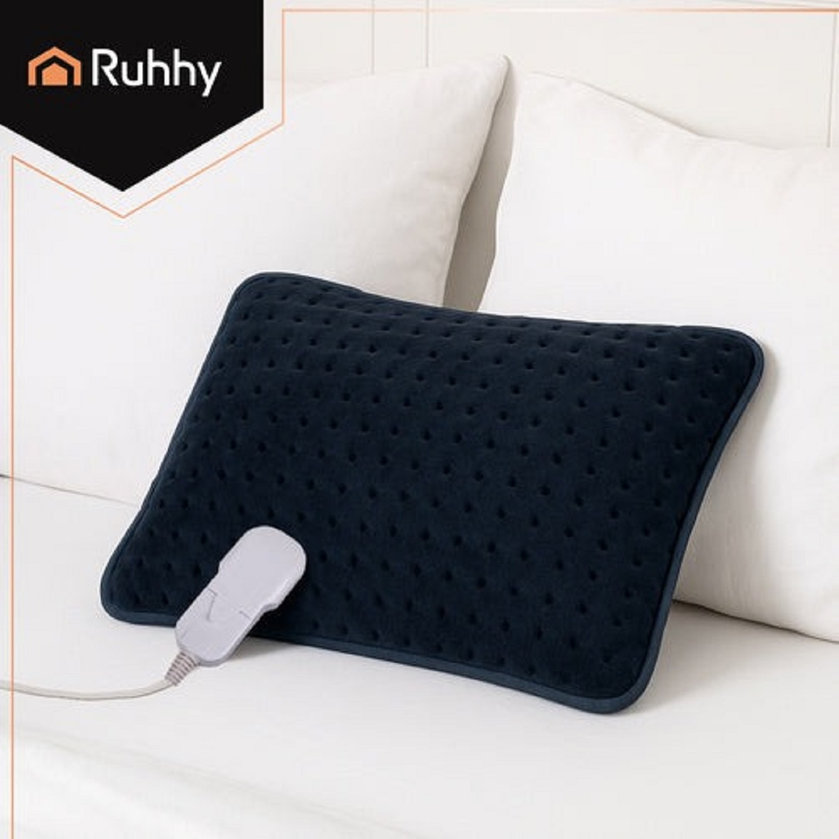 Una almohadilla térmica azul marino con un panel de control está sobre una cama blanca. Dos almohadas blancas en el fondo.