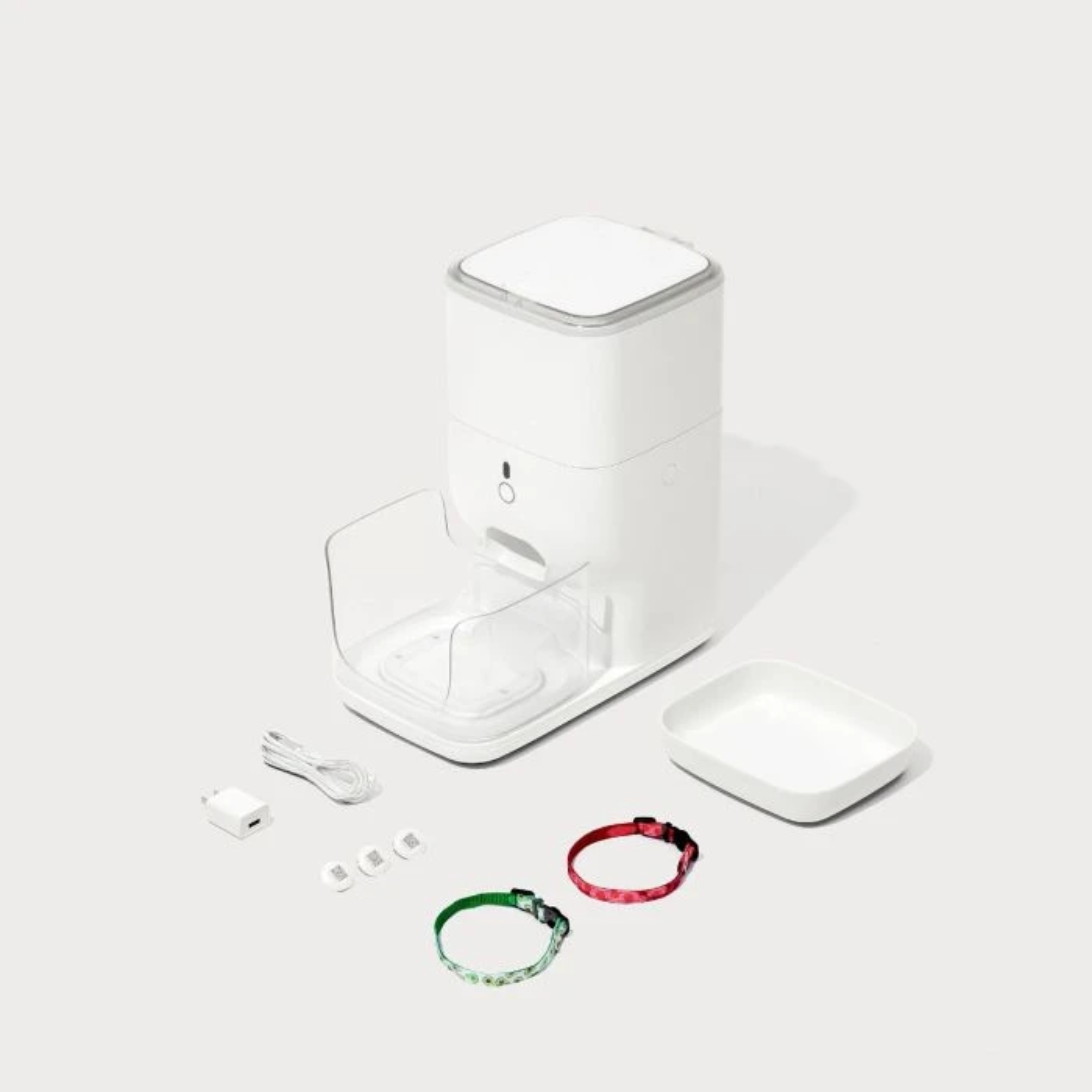 White pet feeder with accessories: charger, collars, and a bowl. The feeder is the main object.
