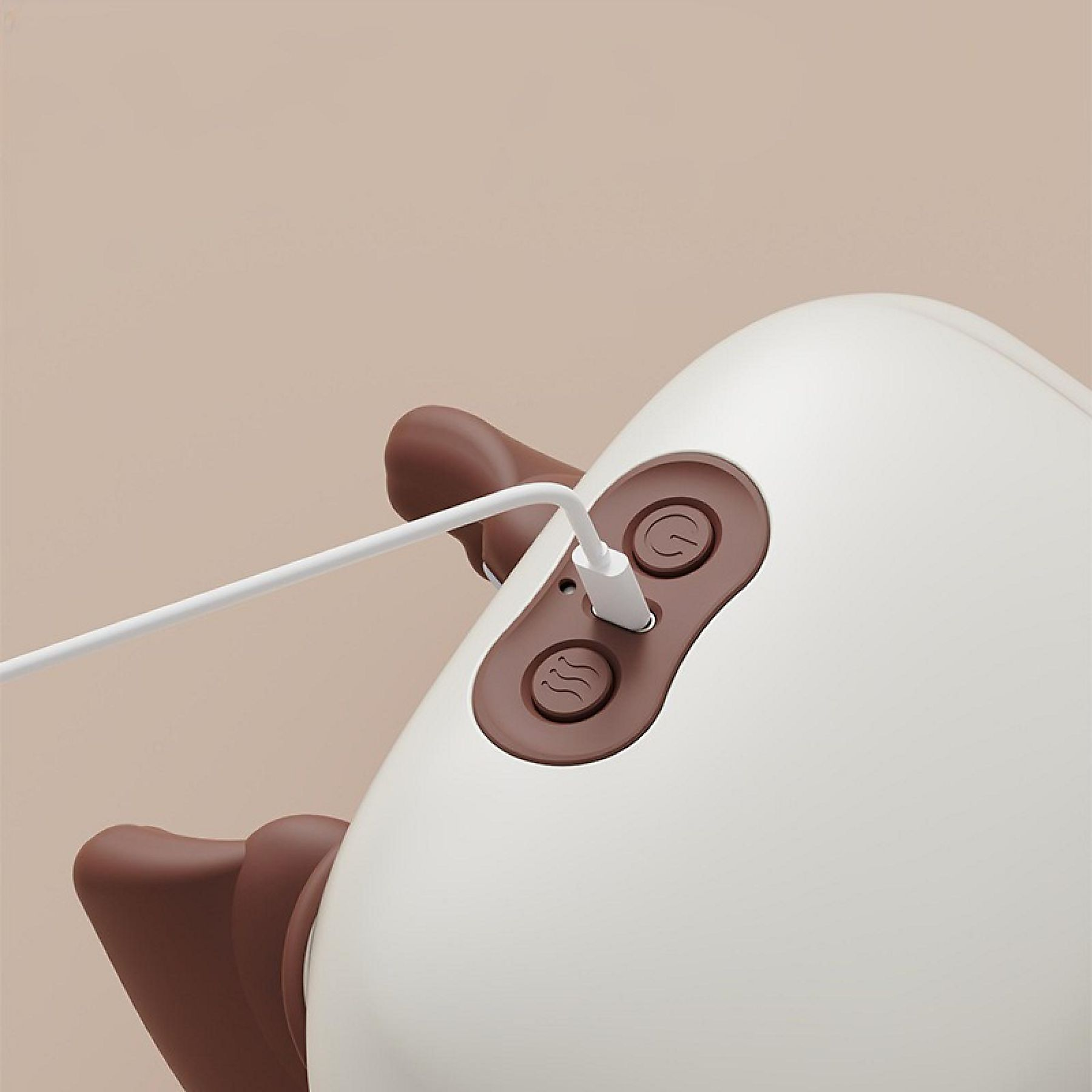 Nahaufnahme eines weißen Geräts mit braunen Knöpfen, ein Ladekabel ist eingesteckt. Der Hintergrund ist beige.