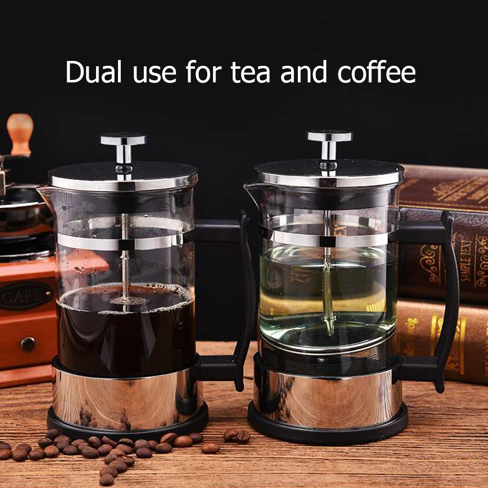 Zwei Glas-Kaffeepressen, eine mit Kaffee, die andere mit Tee. Kaffeebohnen und eine Mühle sind im Hintergrund.