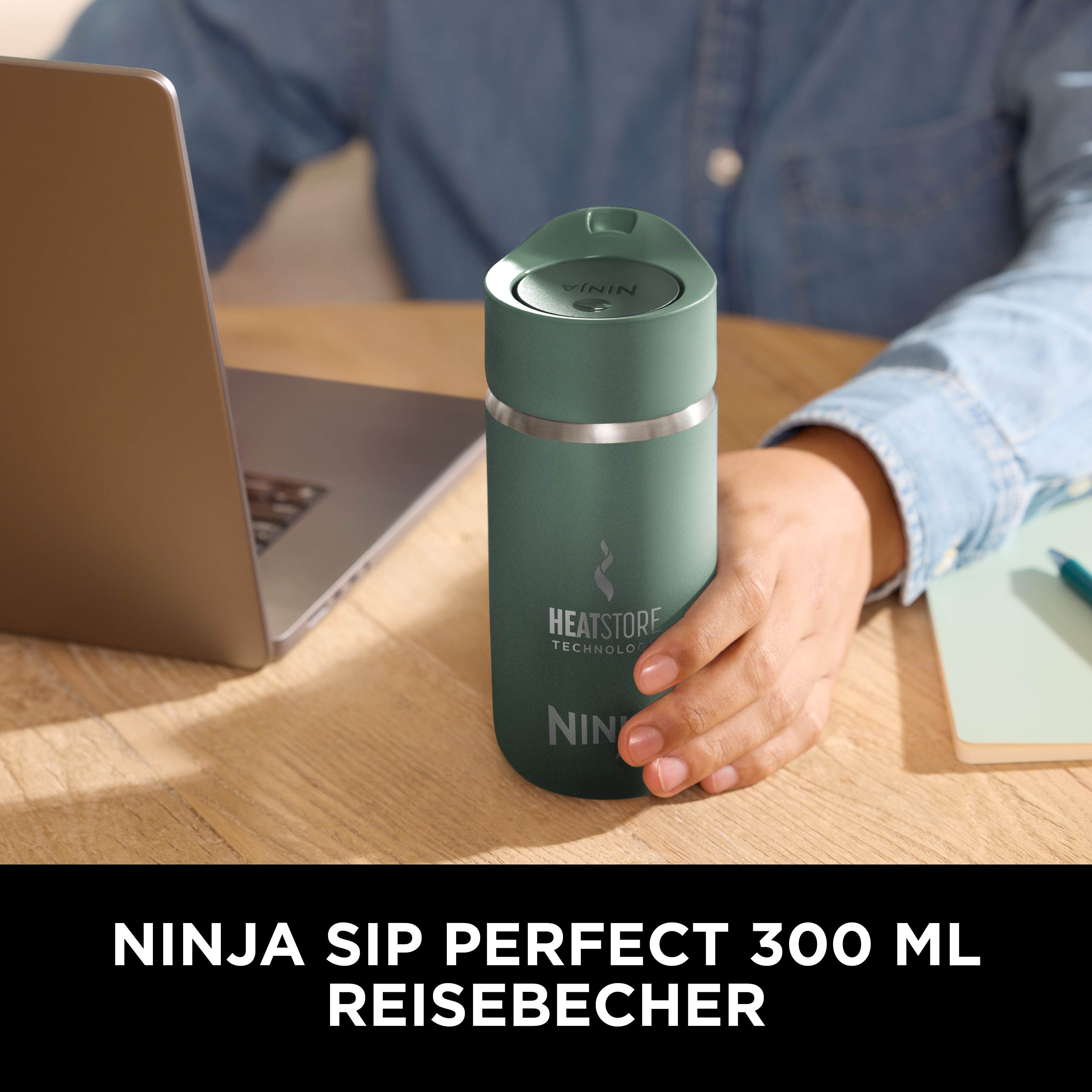 Une personne tient un gobelet de voyage vert près d'un ordinateur portable et d'un bloc-notes. Le texte dit Ninja Sip Perfect 300 ml.