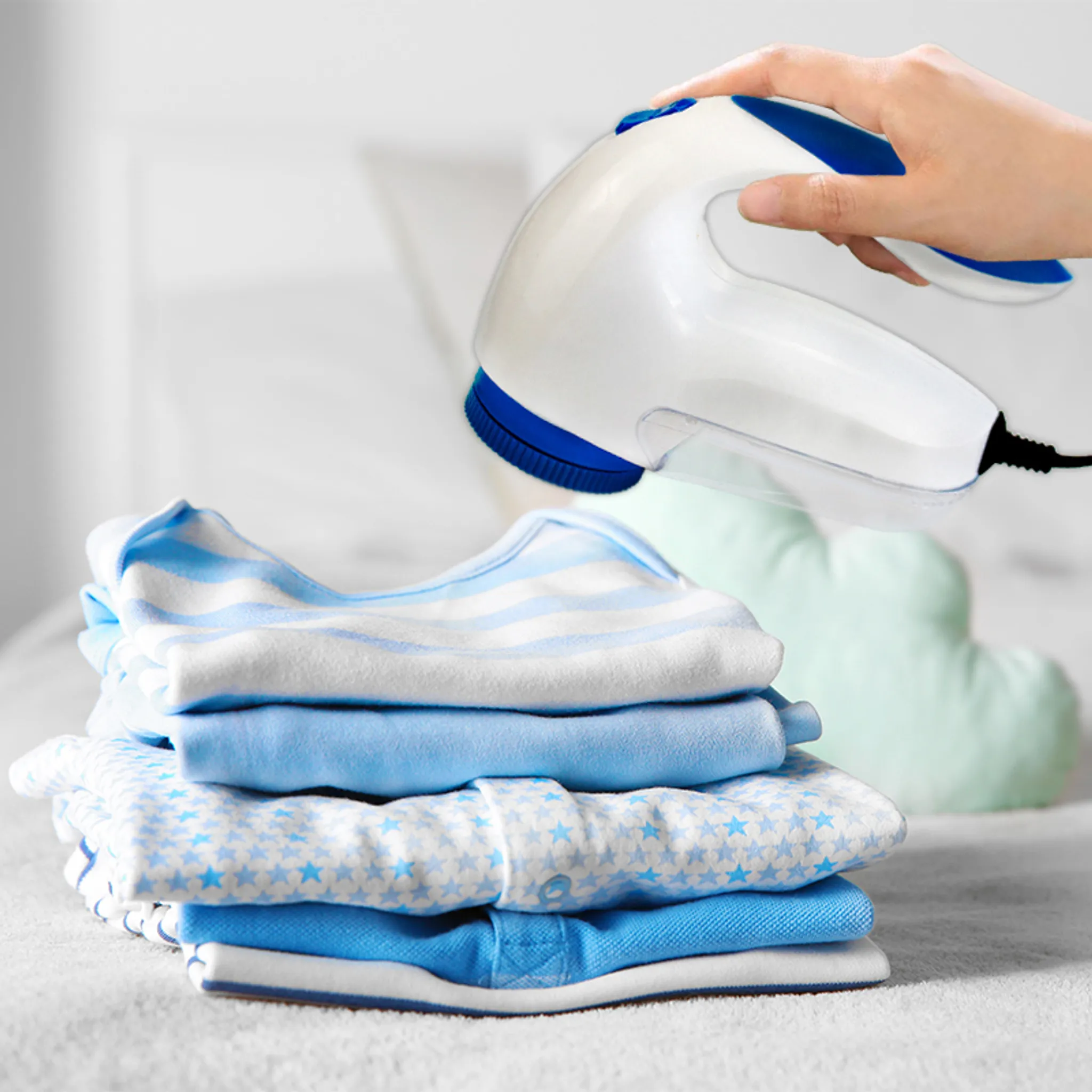 Eine Hand hält einen weißen und blauen Stoffrasierer über einem Stapel blauer Babykleidung.