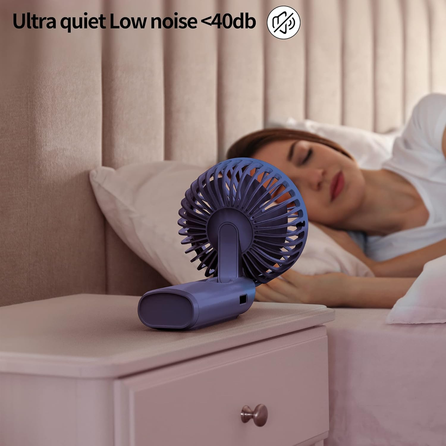 Ein blauer Ventilator steht auf einem Nachttisch neben einer schlafenden Frau im Bett. Die Szene deutet auf eine ruhige, kühle Schlafzimmerumgebung hin.