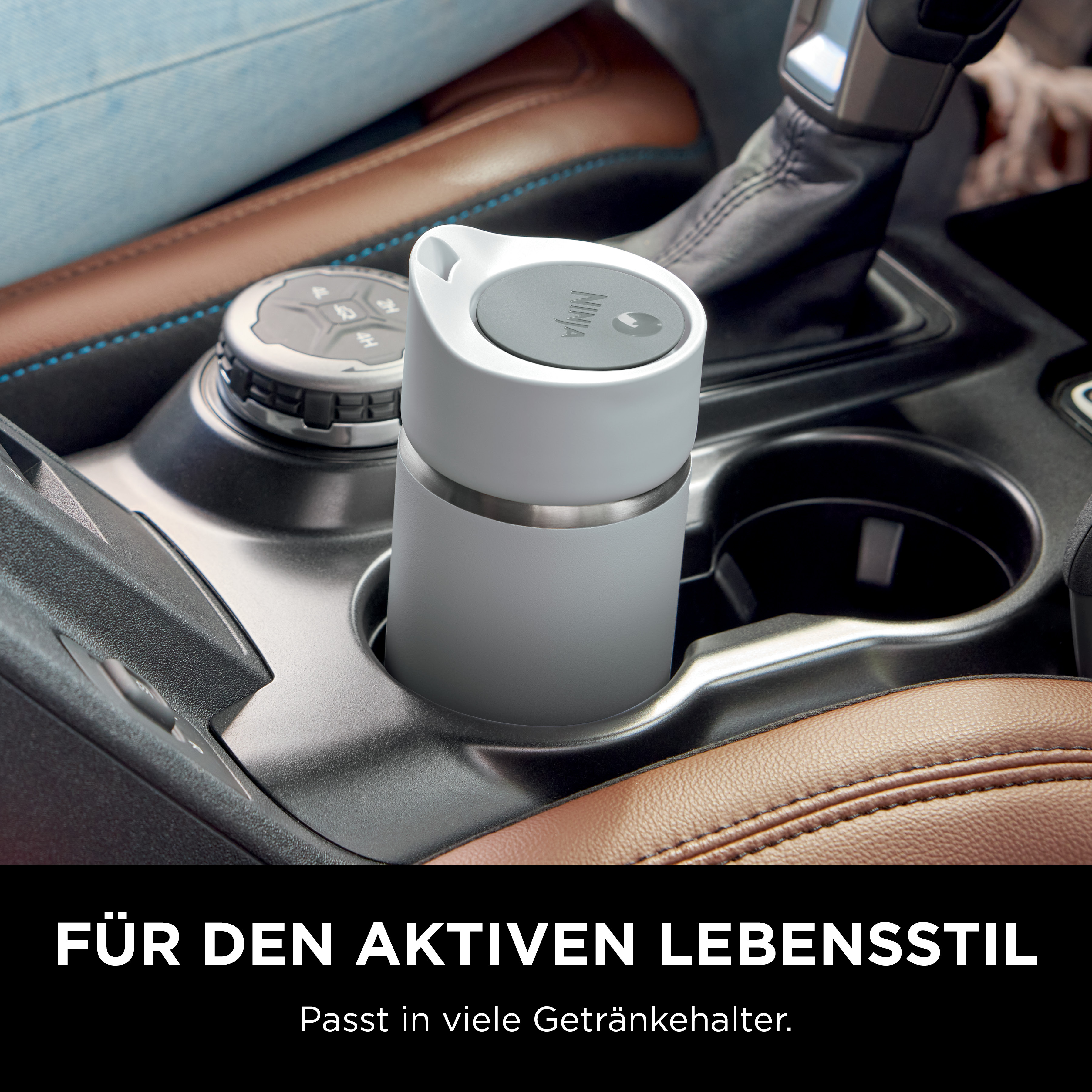 Gobelet gris dans un porte-gobelet de voiture. Sièges en cuir marron et console noire visibles.