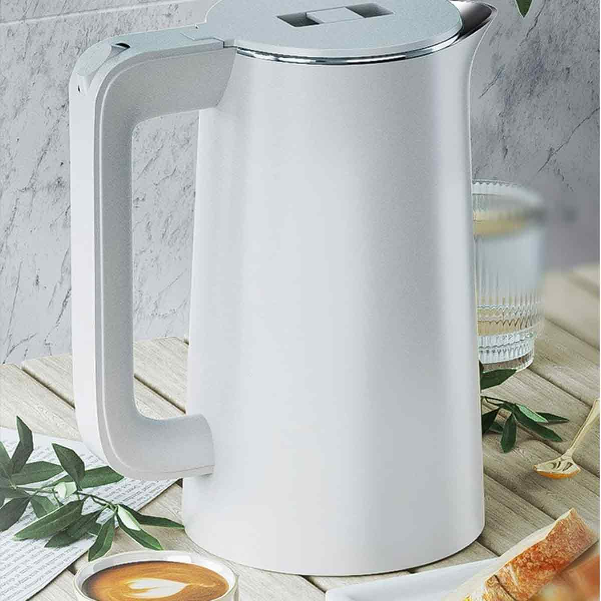 Ein weißer Wasserkocher auf einem Holztisch. Eine Tasse Kaffee, ein Glas Wasser und Brot sind ebenfalls sichtbar.