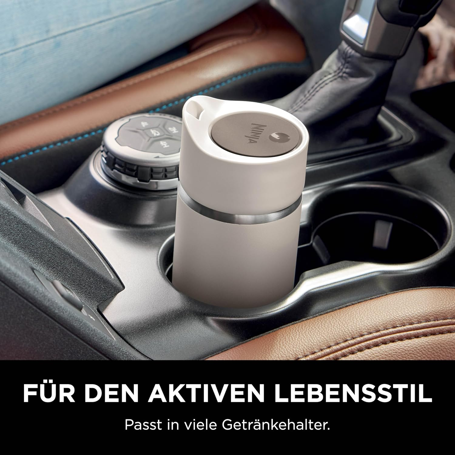 Une tasse de voyage Ninja est dans le porte-gobelet d'une voiture. L'intérieur de la voiture est visible, avec sièges en cuir et levier de vitesse.