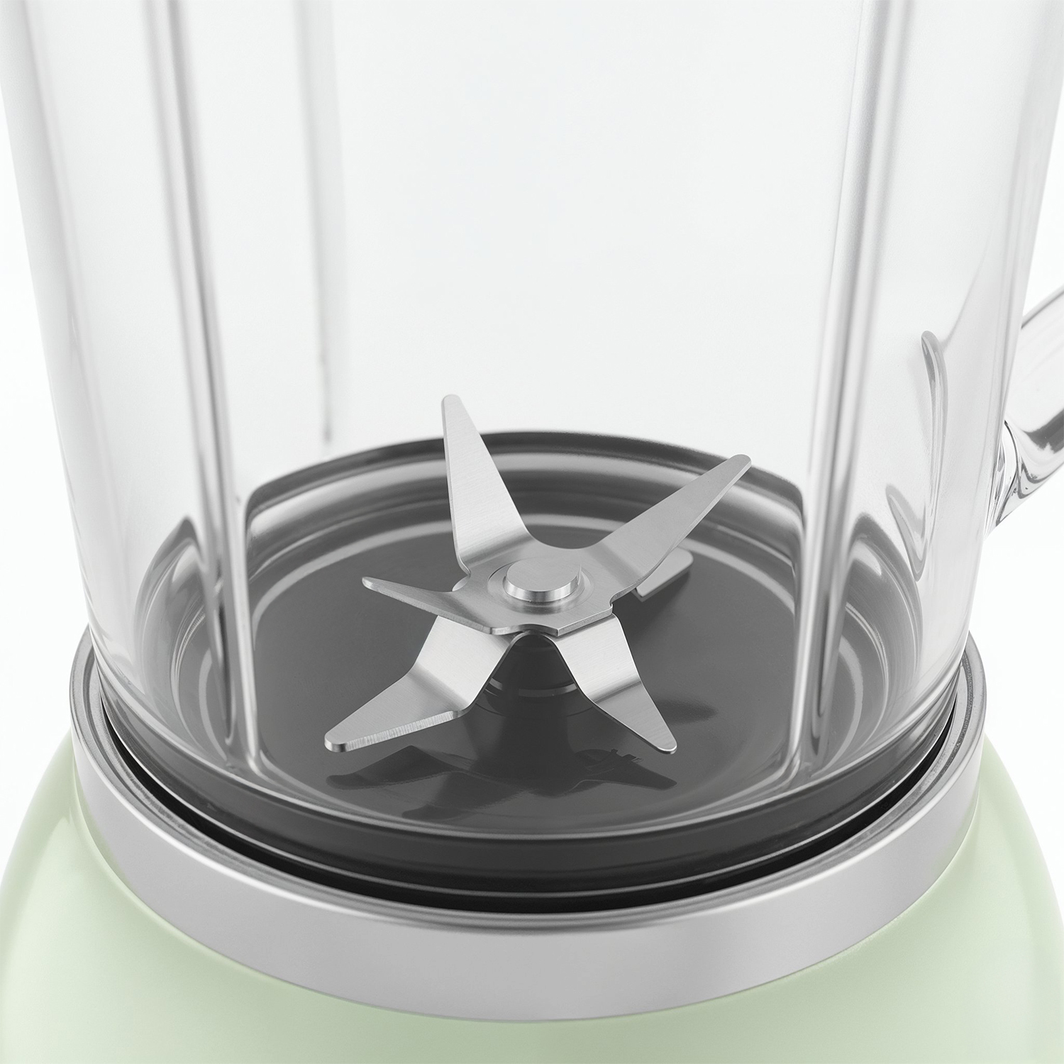 Primer plano de una licuadora. Una cuchilla de acero inoxidable en el centro, con un recipiente de vidrio transparente encima. La base es verde claro.