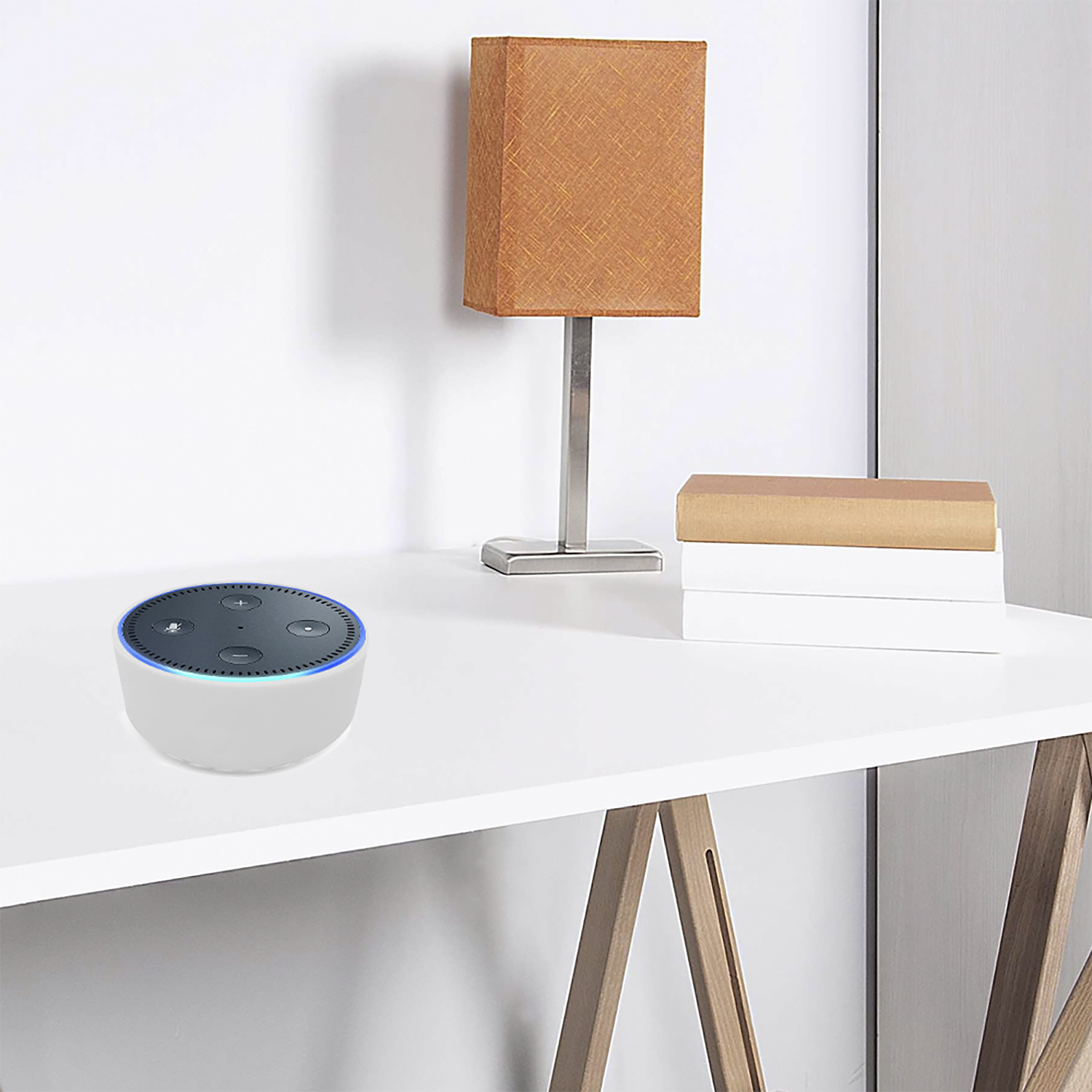 Una scrivania bianca con un Echo Dot, una lampada e dei libri. La lampada ha un paralume marrone. L'Echo Dot è bianco e nero.