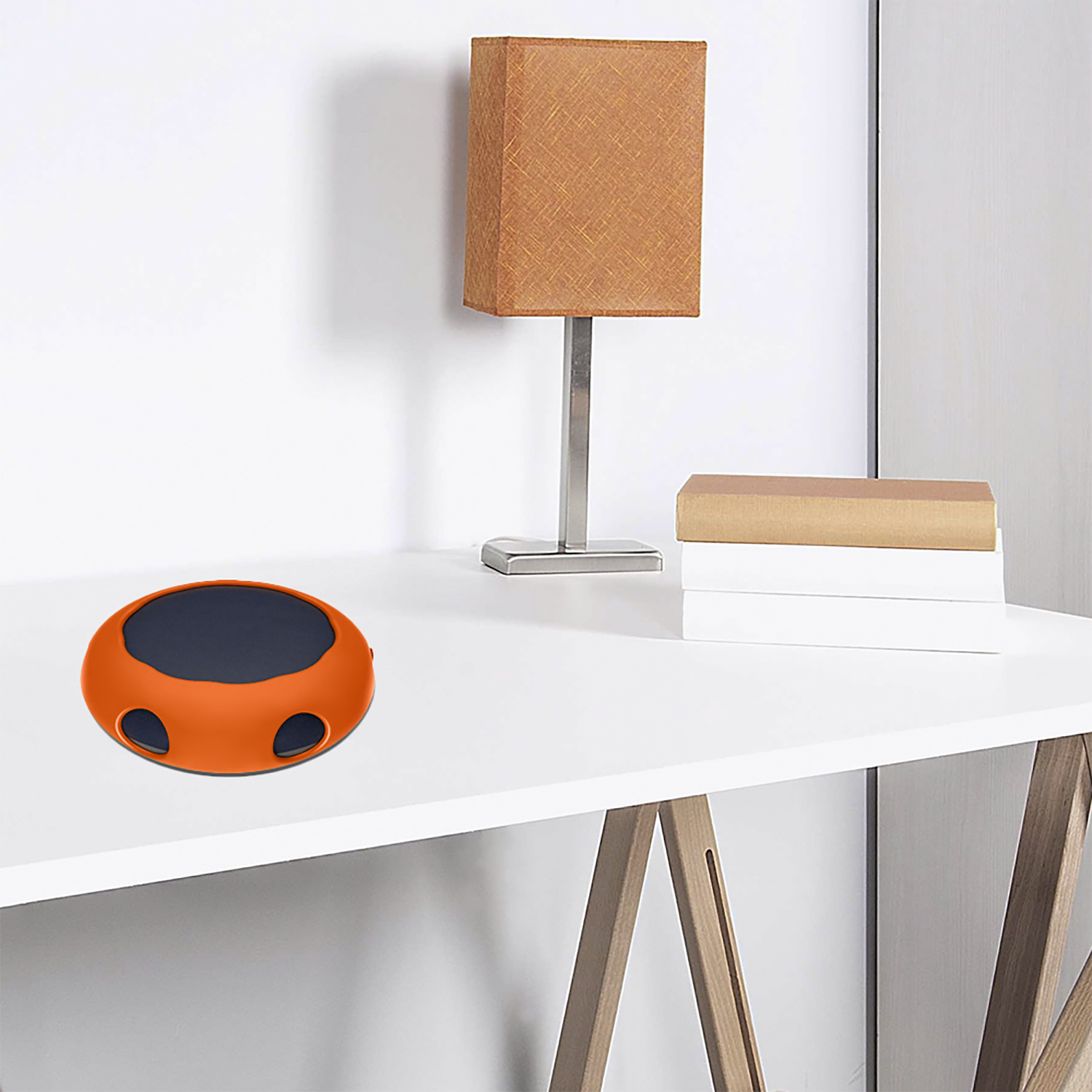Ein orange-schwarzer Lautsprecher steht auf einem weißen Schreibtisch. Eine Lampe und Bücher sind im Hintergrund.