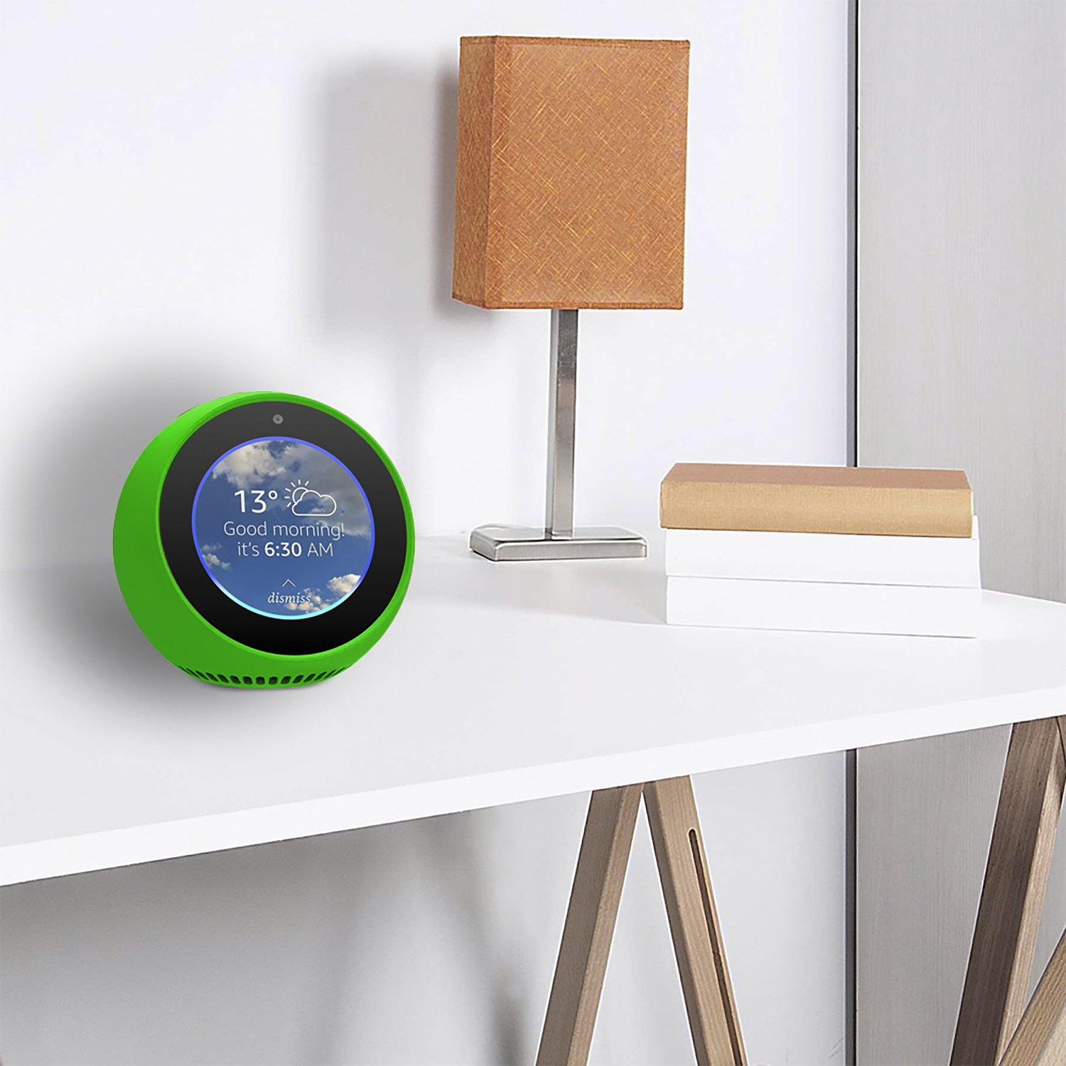 Un altoparlante intelligente verde mostra informazioni meteo. Una lampada arancione e libri sono su un tavolo bianco. Parete bianca sullo sfondo.