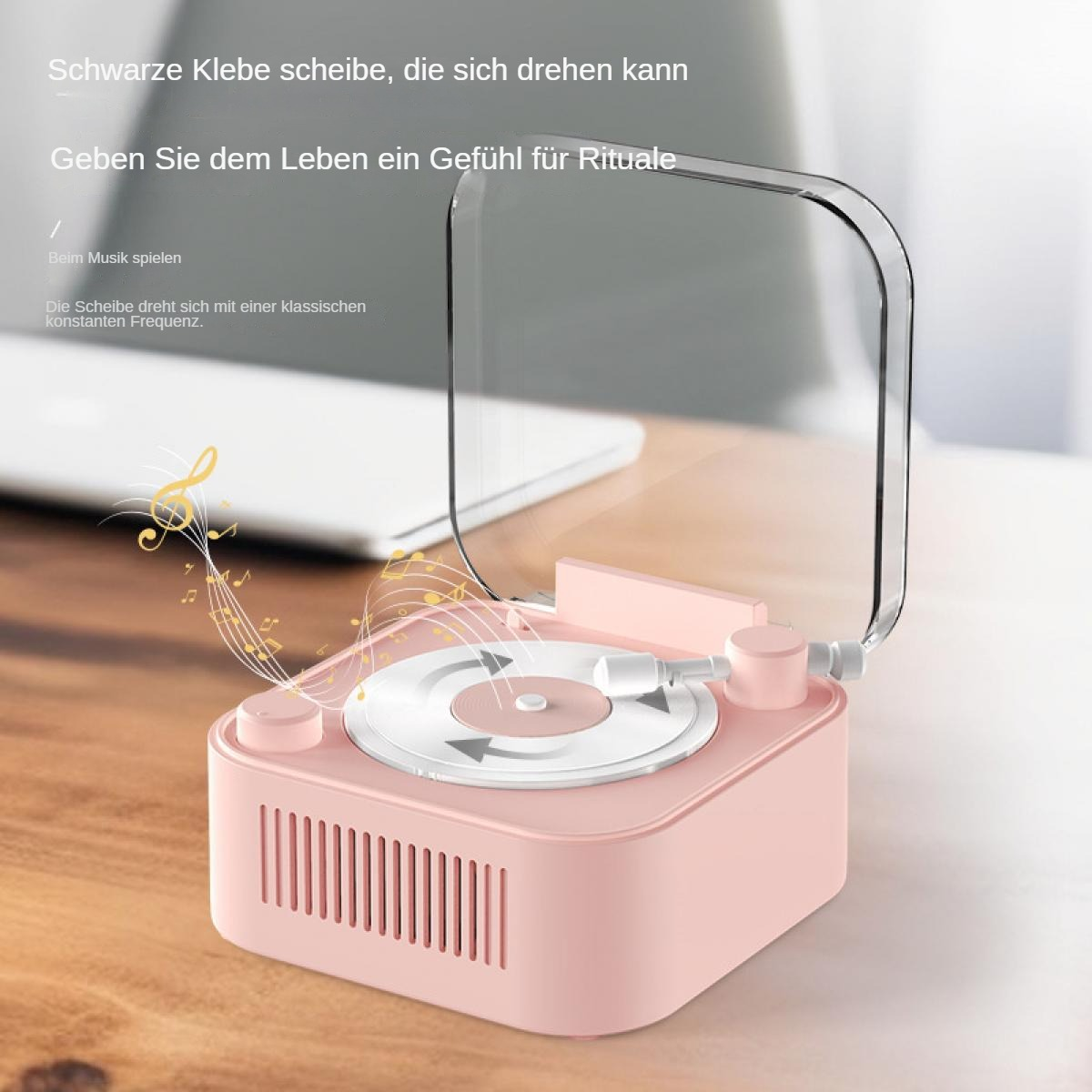 Ein rosa, miniaturisierter Plattenspieler mit einer durchsichtigen Abdeckung steht auf einer Holzoberfläche. Noten gehen davon aus.