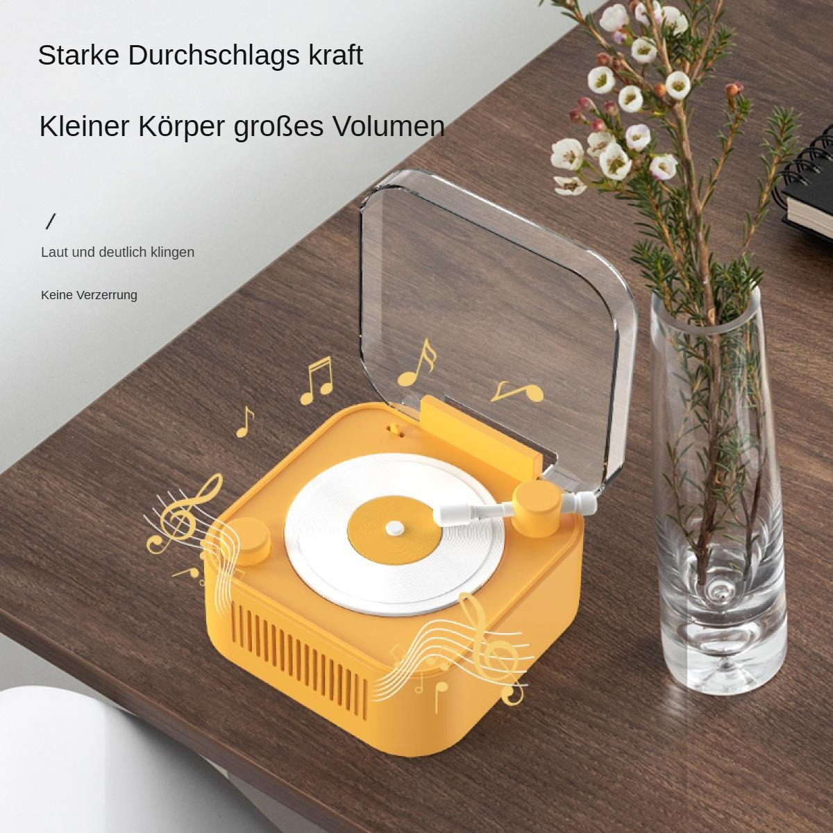 Ein orangefarbener Plattenspieler mit klarer Abdeckung, eine Vase mit Blumen und Noten auf einem Holztisch. Text auf Deutsch.
