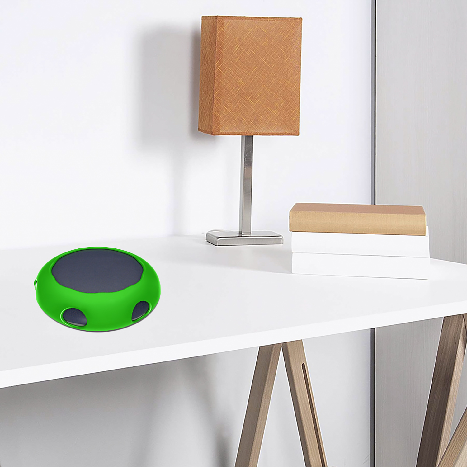 Un dispositivo verde e grigio su una scrivania bianca. Sono visibili anche una lampada, libri e una gamba del tavolo in legno.