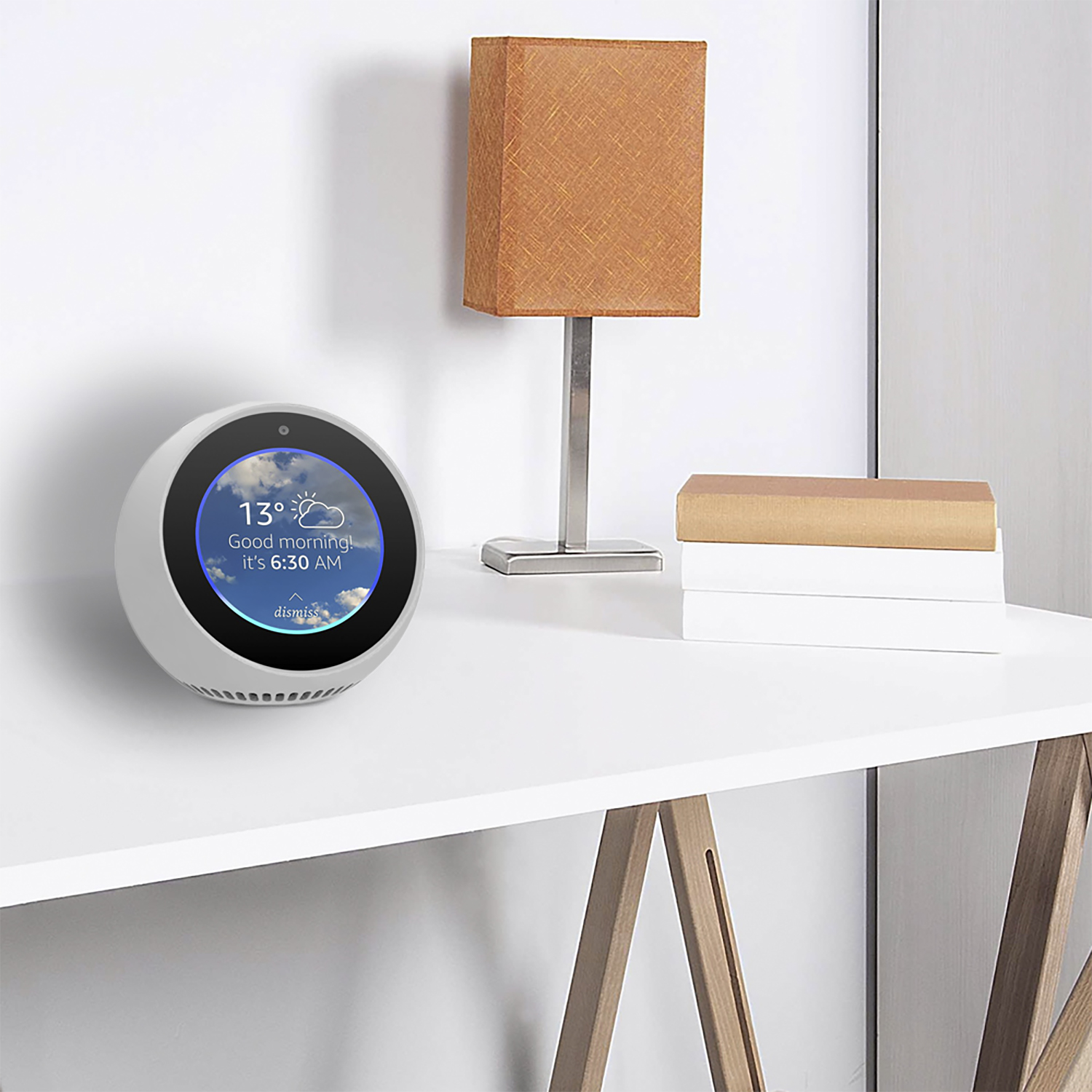 Smart display mostra il meteo. Lampada arancione e libri su un tavolo bianco. Parete bianca sullo sfondo.