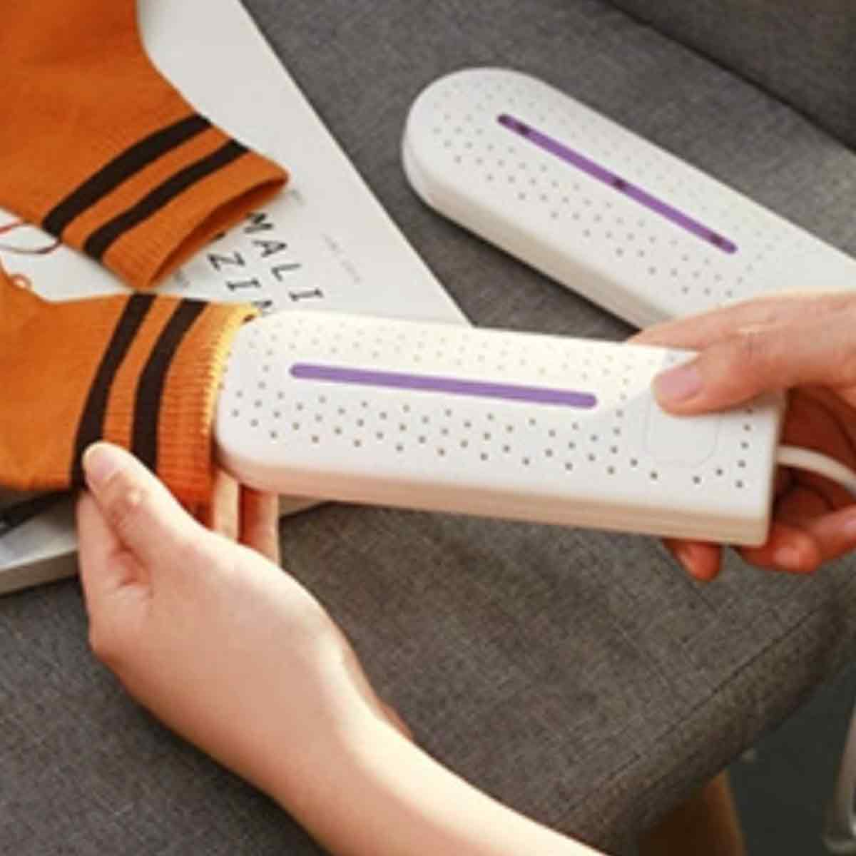 Eine Person benutzt einen weißen Sockenrockner mit einer lila Linie auf einer orangefarbenen Socke mit schwarzen Streifen. Ein anderer Trockner ist daneben.