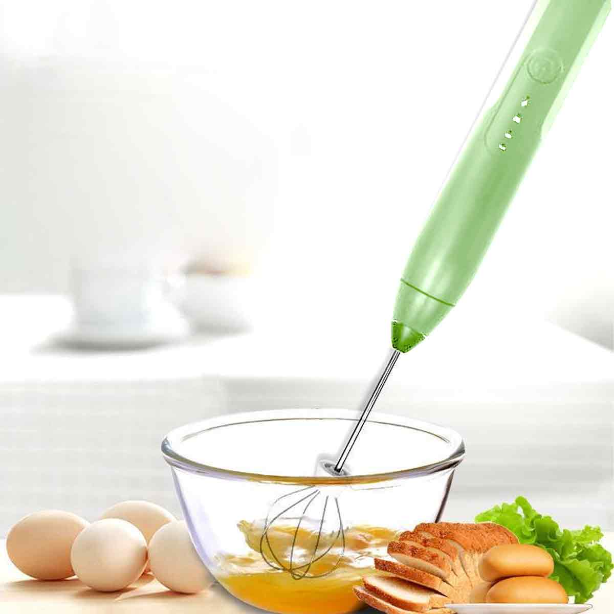 Ein grüner Handmixer verrührt Eier in einer Glasschüssel. Eier, Brot und Salat sind im Vordergrund. Weißer Hintergrund.