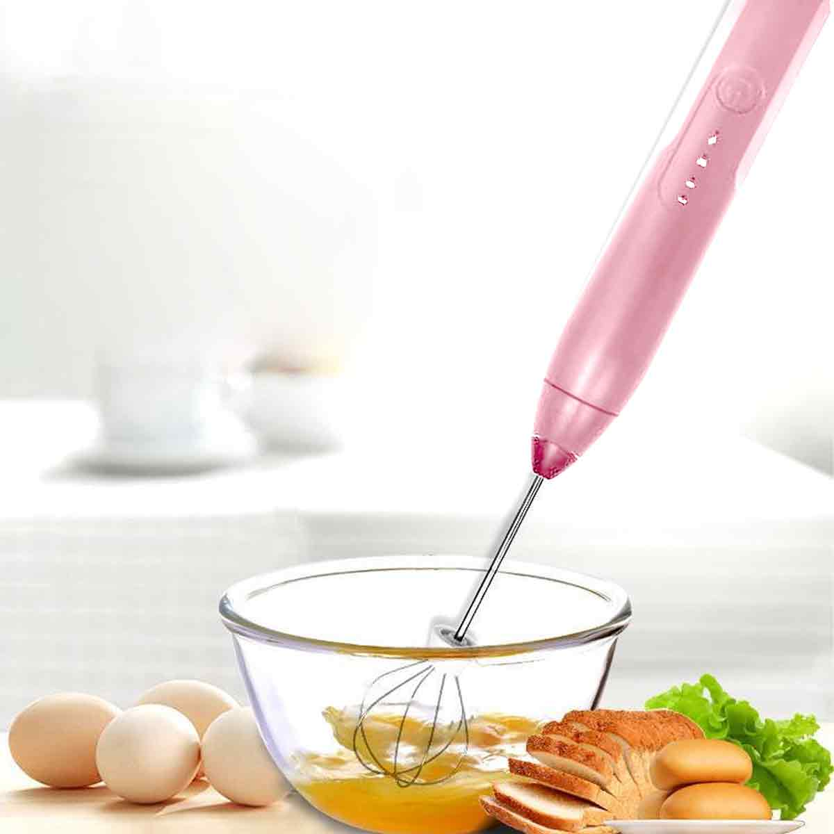 Ein pinkfarbener Handmixer verrührt Eier in einer Glasschüssel. Eier, Brot und Salat liegen neben der Schüssel.