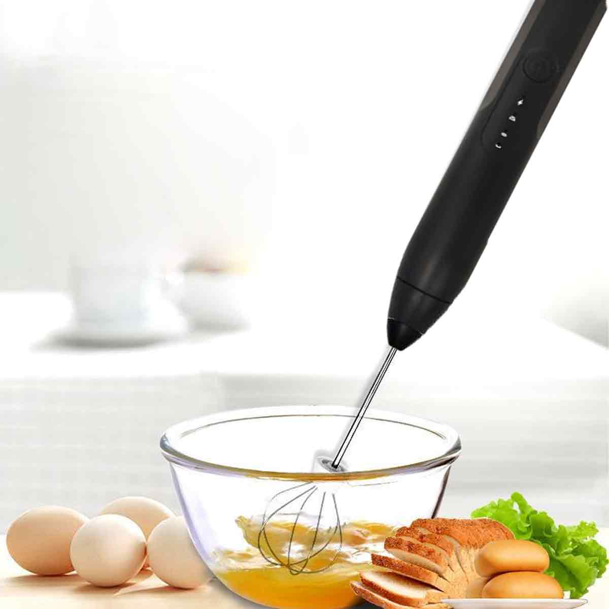 Ein schwarzer Handmixer verrührt Eier in einer Glasschüssel. Eier, Brot und Salat liegen neben der Schüssel.