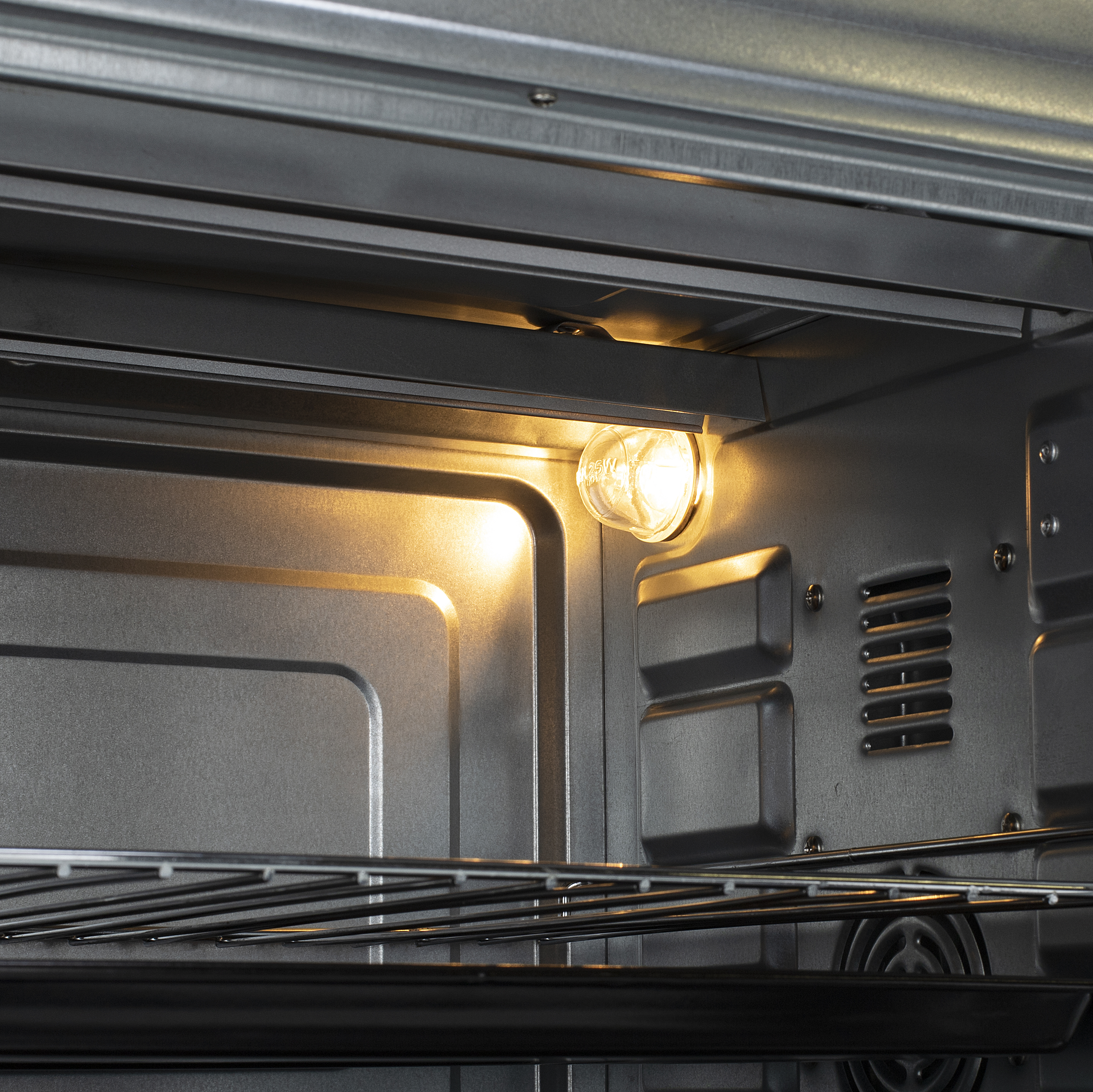 All'interno di un forno, una lampadina brilla. Pareti e griglie metalliche sono visibili, riflettendo la luce calda.