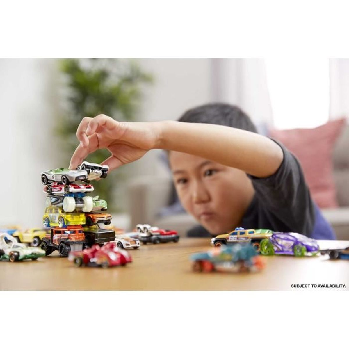 Un niño apila coches de juguete en una mesa. Varios coches coloridos están dispersos. La mano del niño está cerca de la parte superior.