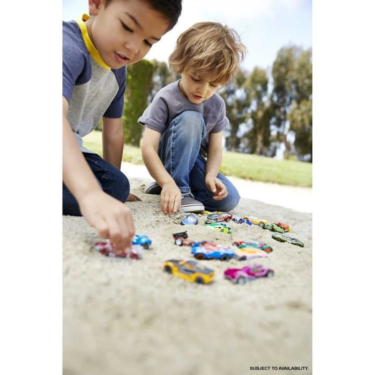 Dos niños juegan con coches de juguete en la arena. Uno está arrodillado y el otro sentado. Coches de muchos colores en la arena.