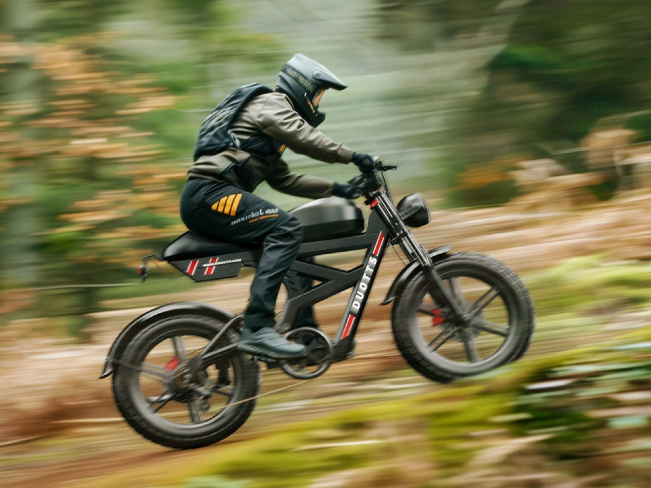 Una persona guida una moto elettrica nera su un sentiero forestale. La bici ha dettagli rossi e il pilota indossa casco e zaino.