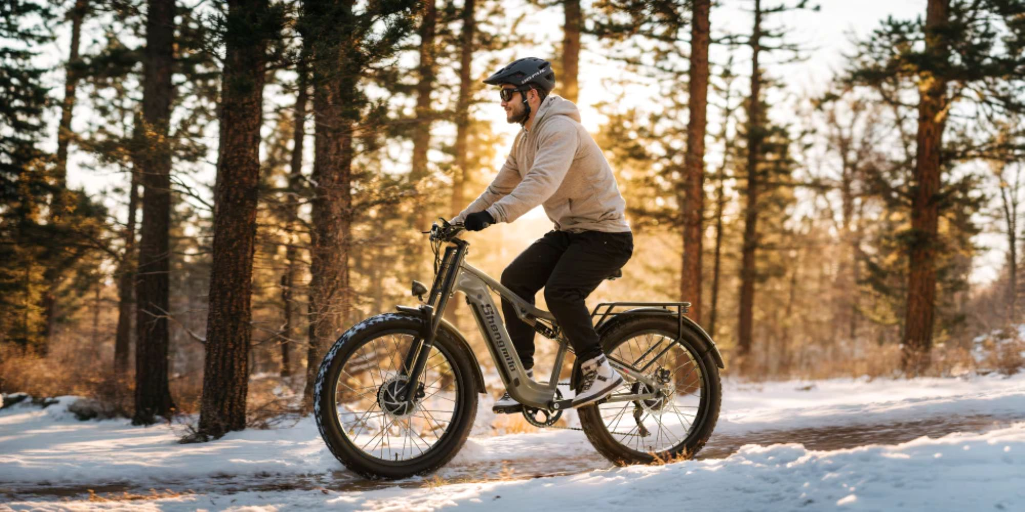 Uomo in sella a una e-bike su un sentiero innevato in una foresta. La bici è grigia. Gli alberi sono sullo sfondo.